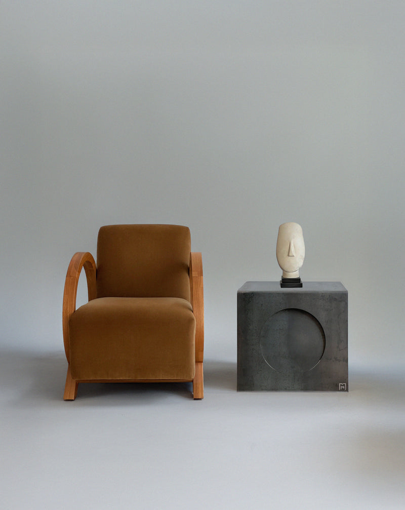 Era concrete side table with circular cutout by Modan next to brown velvet armchair