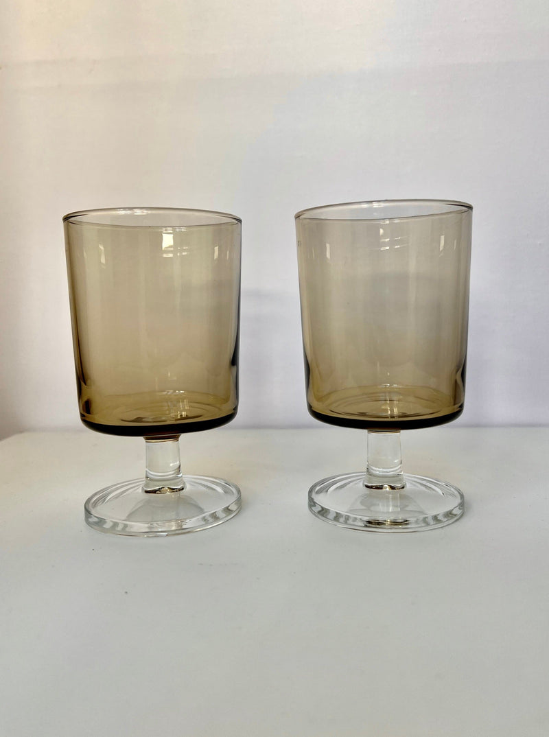 Two amber tinted stem glasses with clear bases on white surface