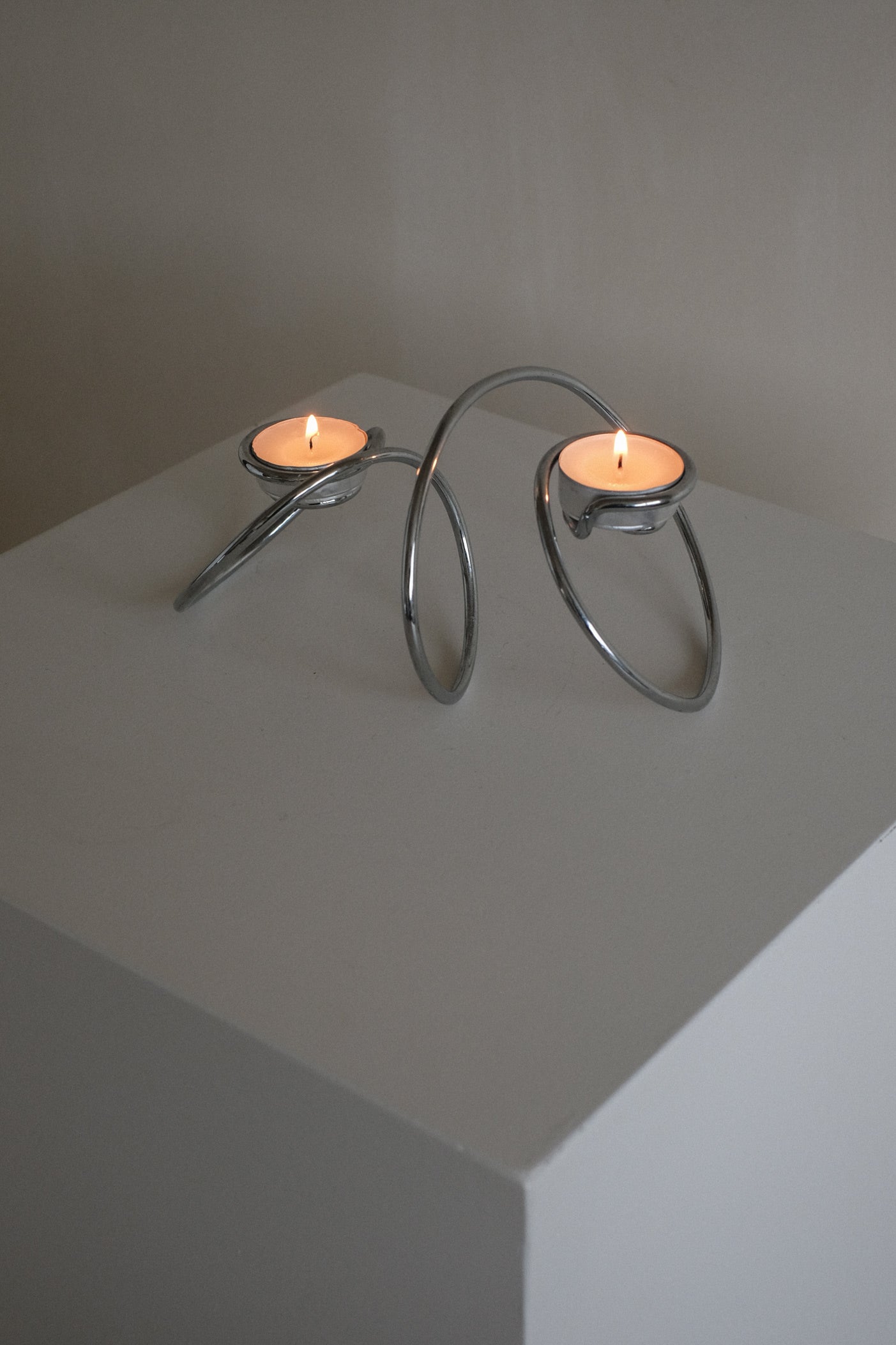 Chrome Candleholder — angled view on white pedestal with candles lit