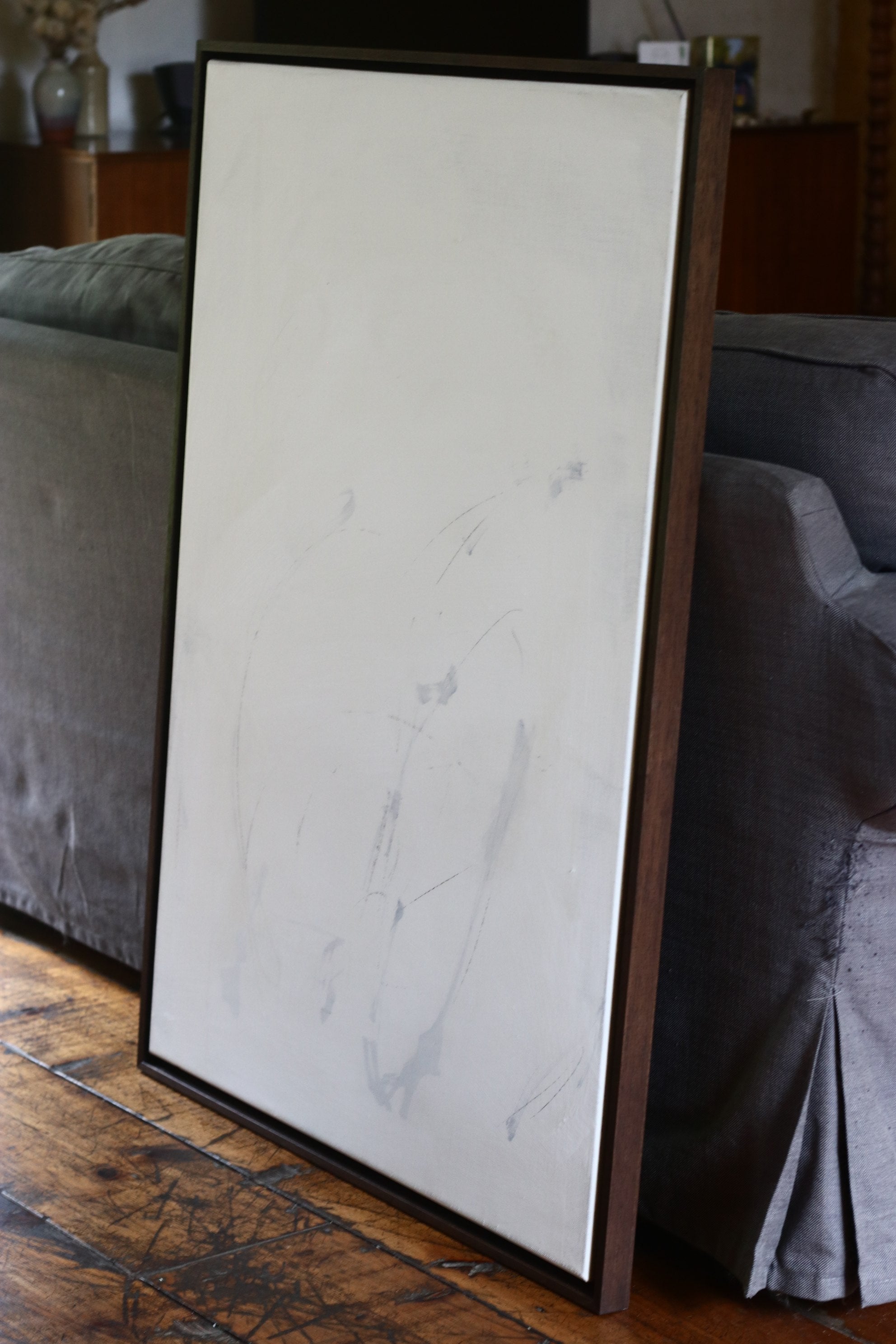 Mixed media abstract painting on linen in wooden frame leaning against sofa
