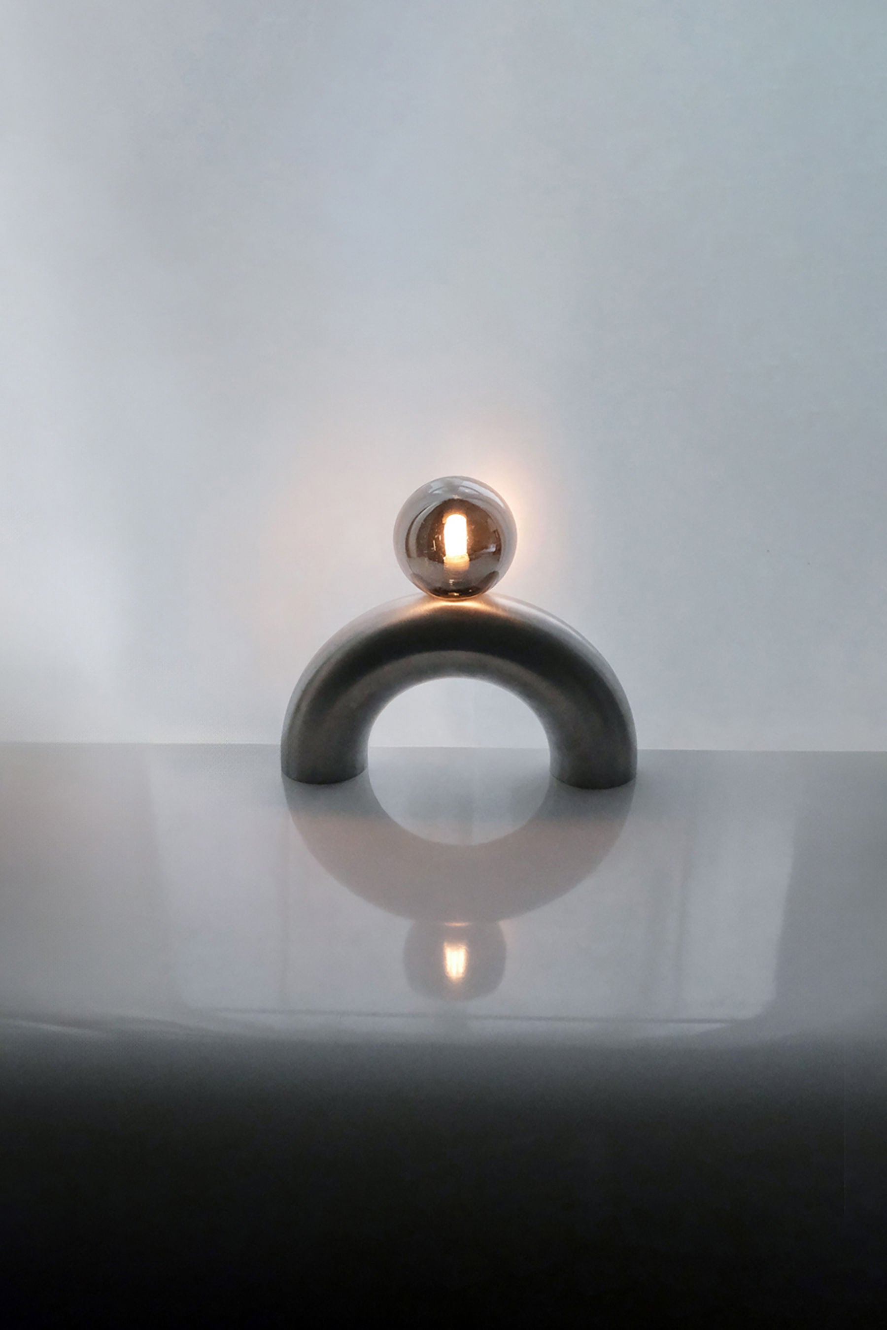 Arcora aluminum arc lamp with illuminated glass sphere on reflective surface