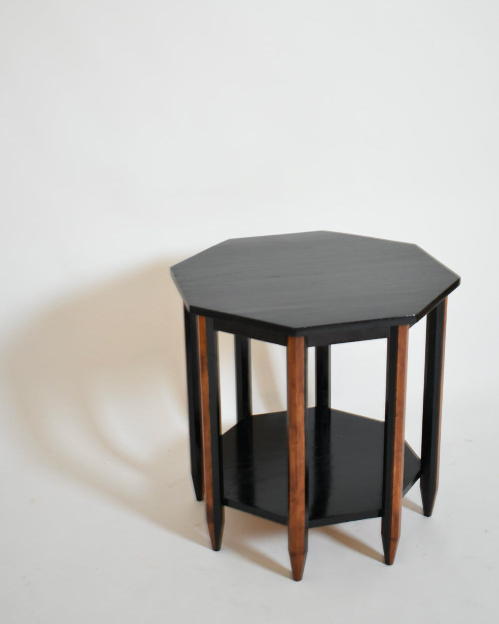 The Octogonal Modernist Side Table, 1920s by Barracuda Interiors features a black octagonal top, wooden legs, and an open lower shelf, shown against a plain white background.