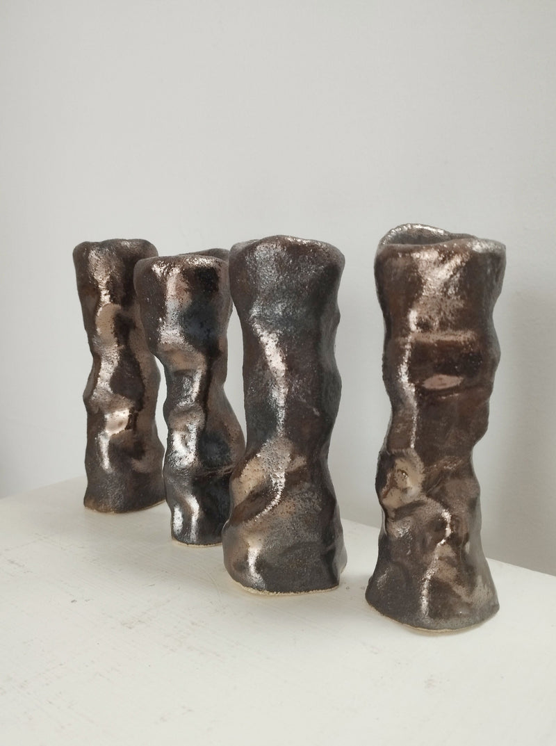 The Claire Pain Candleholder in sandstone and bronze enamel features a metallic, organically-shaped design with a textured surface, arranged on a white background to resemble decorative ceramic vases or artful candleholders.