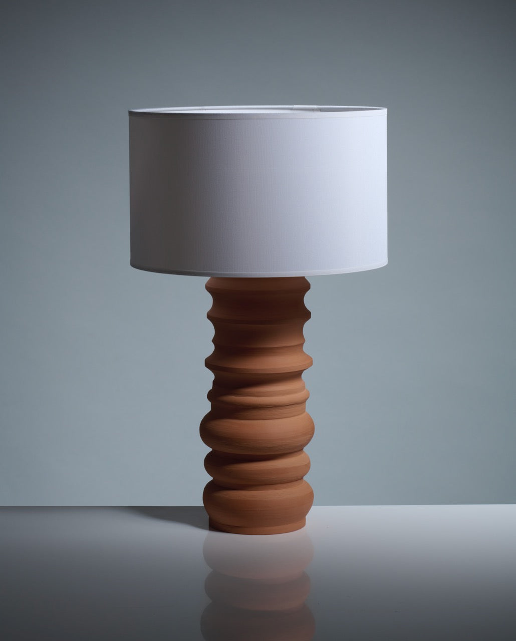 The Katia Langeard Terracotta Glow Table Lamp features a sculpted wavy terracotta ceramic base and a plain white cylindrical shade, perfect for adding modern style to any neutral space.