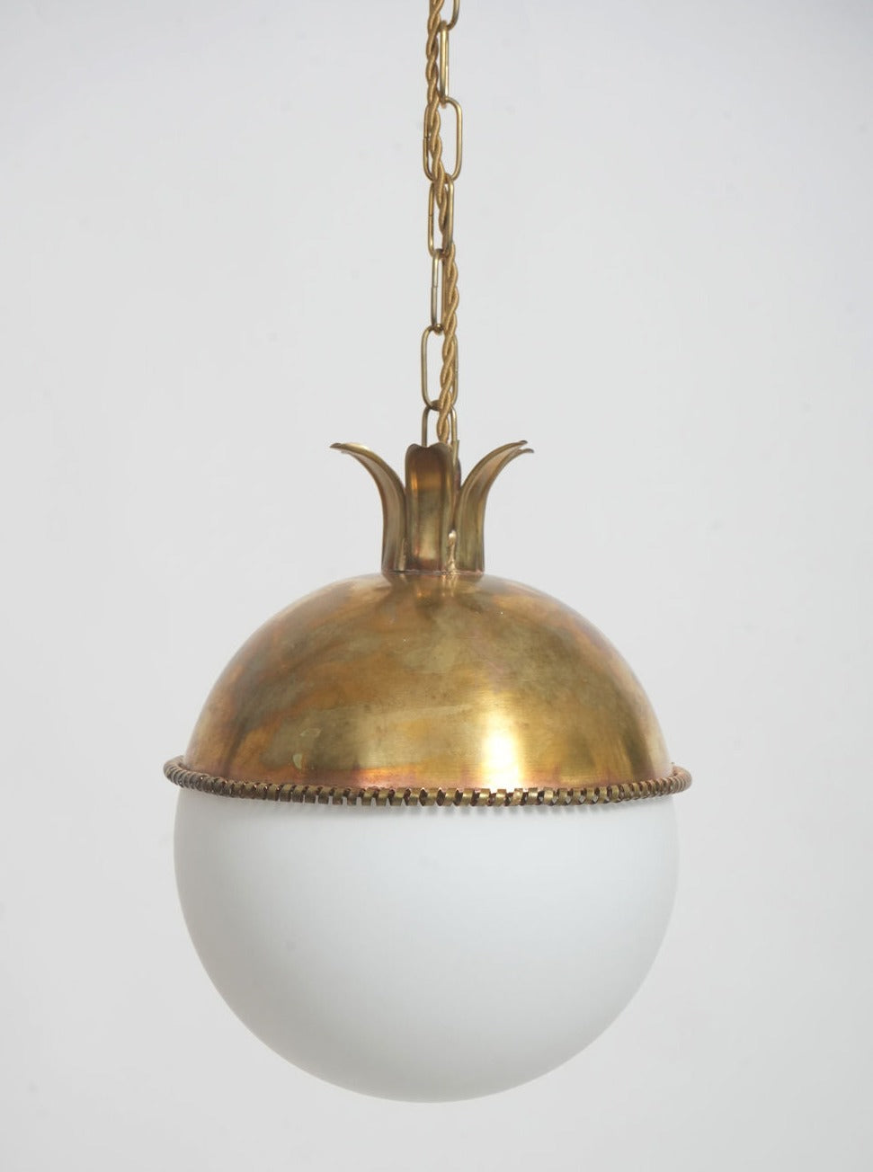 The Granada Ceiling Pendant Lamp by Barracuda Interiors features a frosted white glass globe and a brass crown-like top, elegantly suspended by a brass chain.