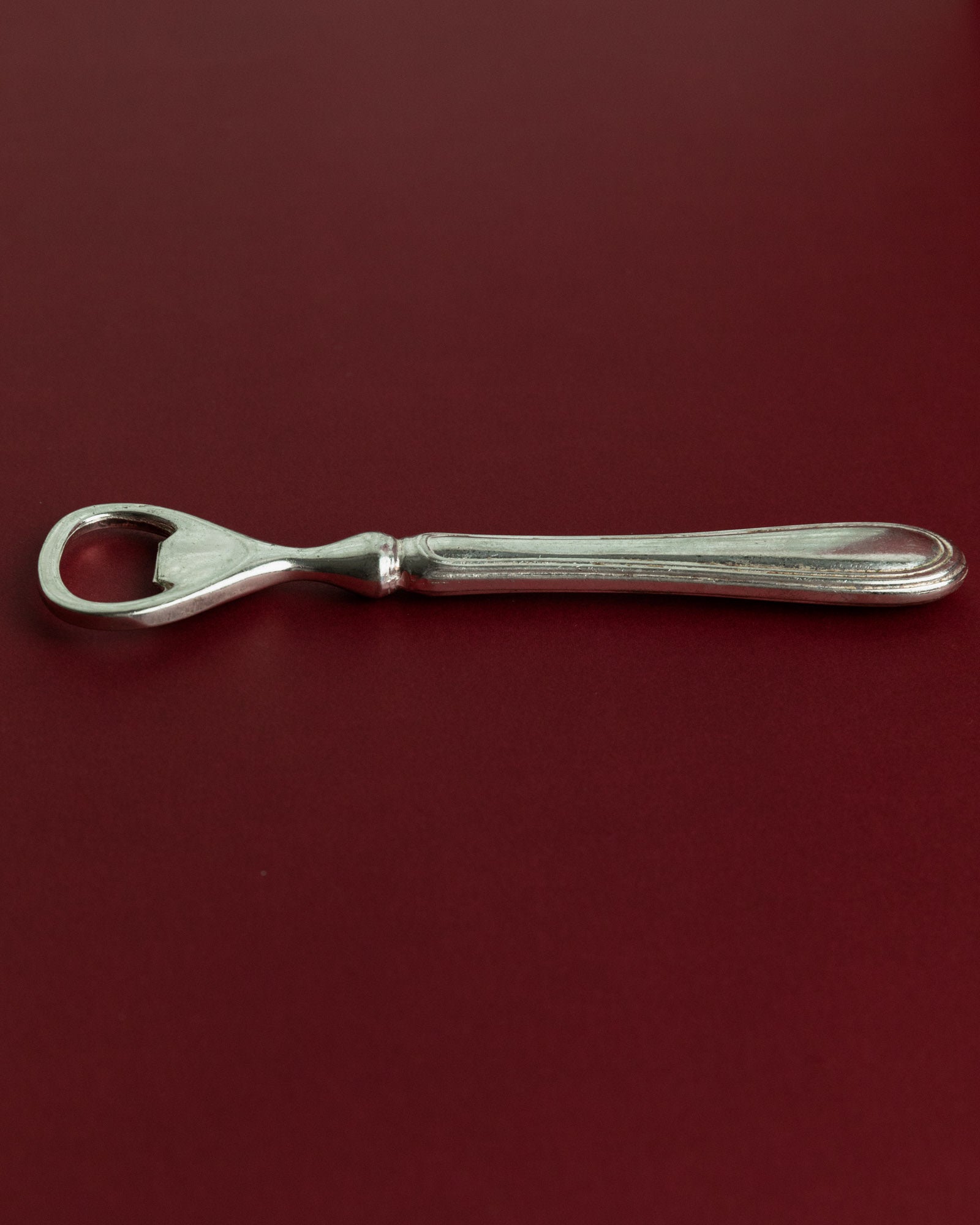 Vintage 1960s Silver Plated Bottle Opener, Classic Minimal Design, Retro Bar Accessory — back view on burgundy background