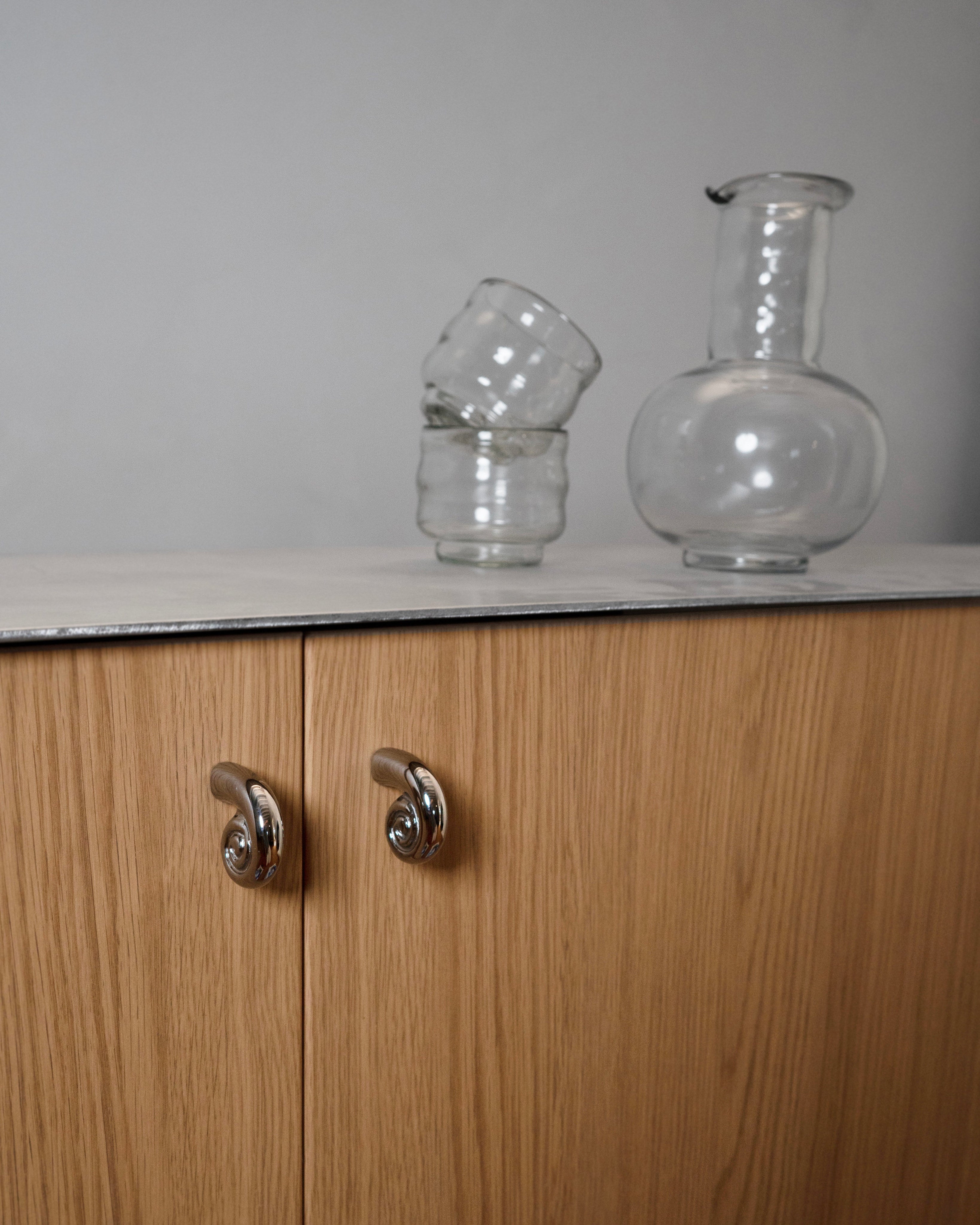 Noelle Knob - Titanium — side view on wooden cabinet with glassware
