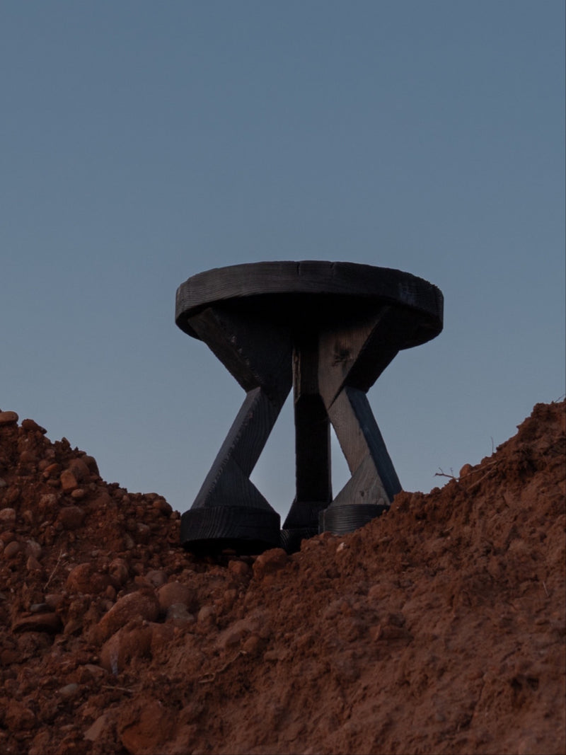 ABORA burnt wood end table with sculptural tripod legs on earthen ground