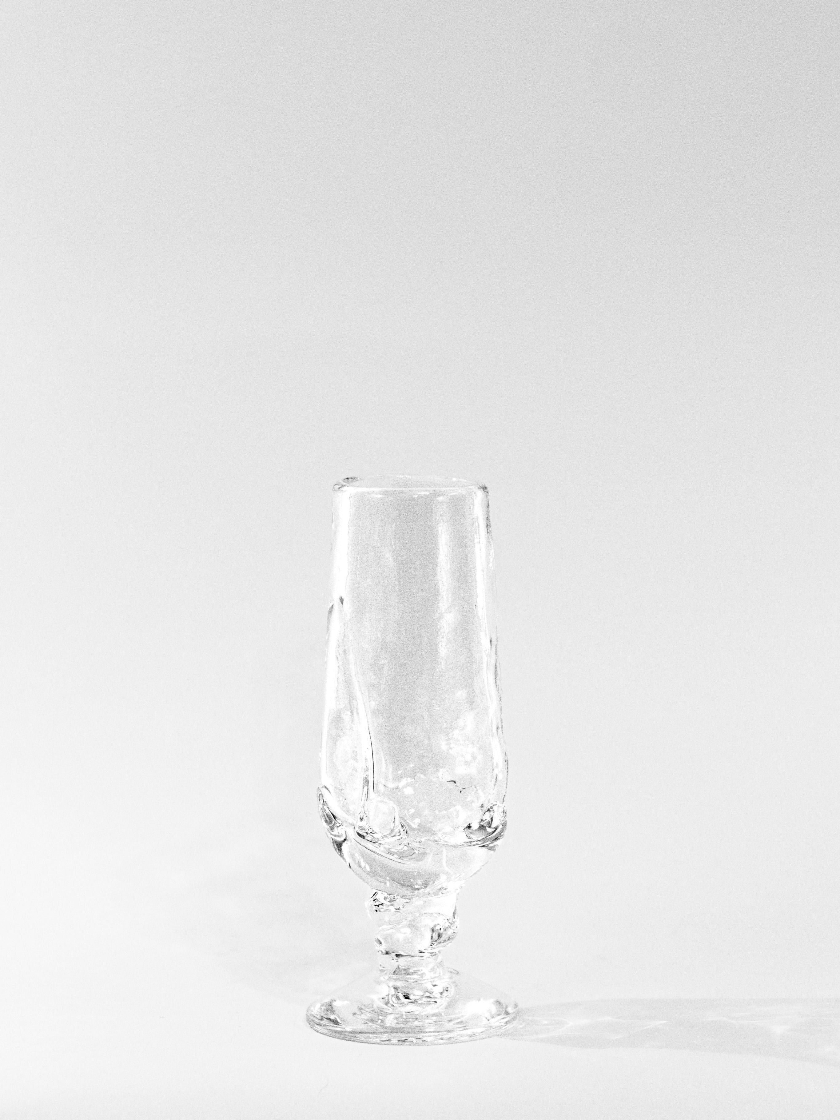 A clear, empty Table Goblet by Szkło Studio stands upright on a white surface with a faint right-side shadow. The simple background highlights the elegance of traditional glass-blowing craftsmanship.