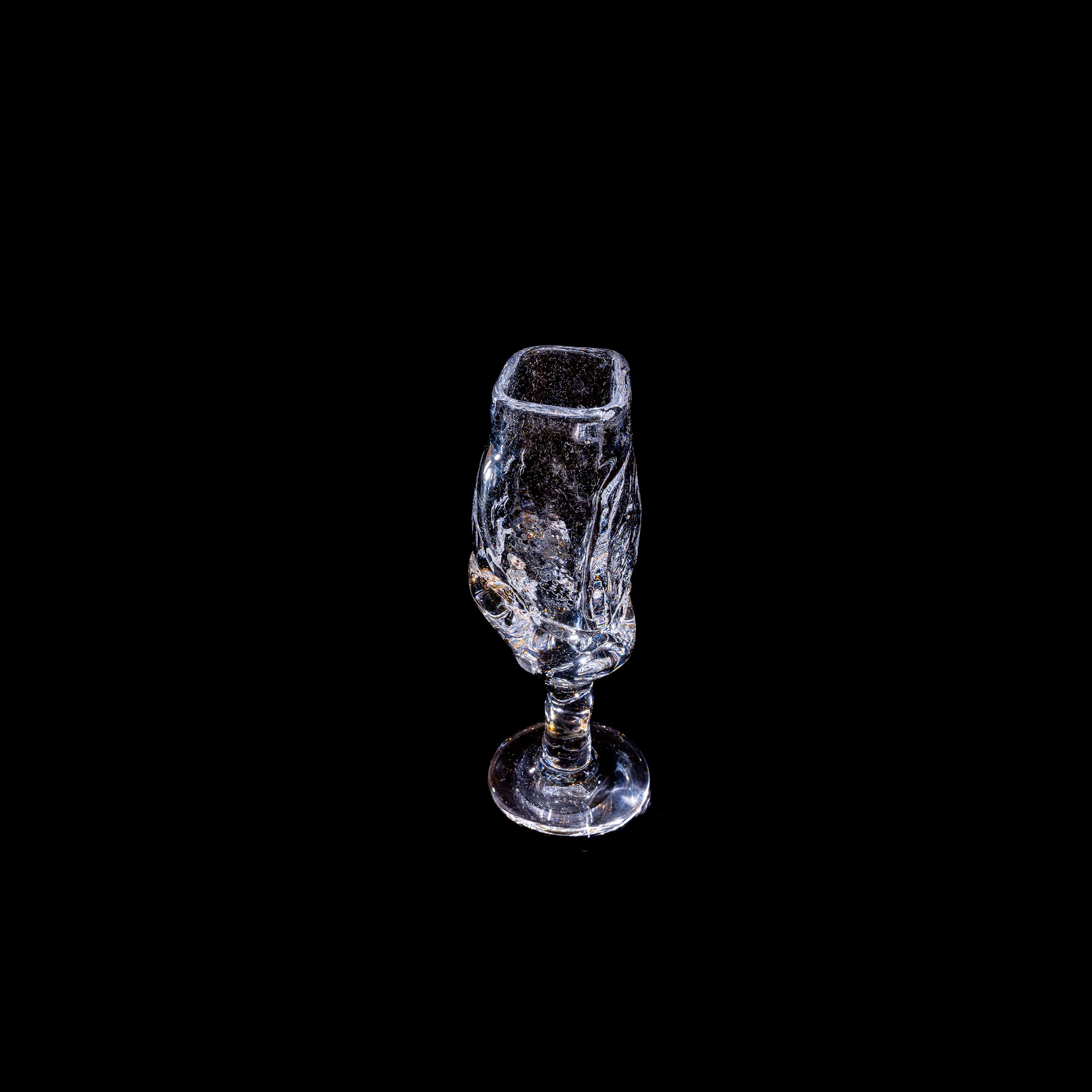 A clear, intricately designed Szkło Studio Table Goblet stands upright against a solid black background, showcasing its decorative patterns and expert glassblowing craftsmanship.
