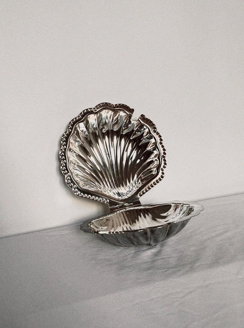 Silver shell-shaped butter dish with ornate beaded rim on marble