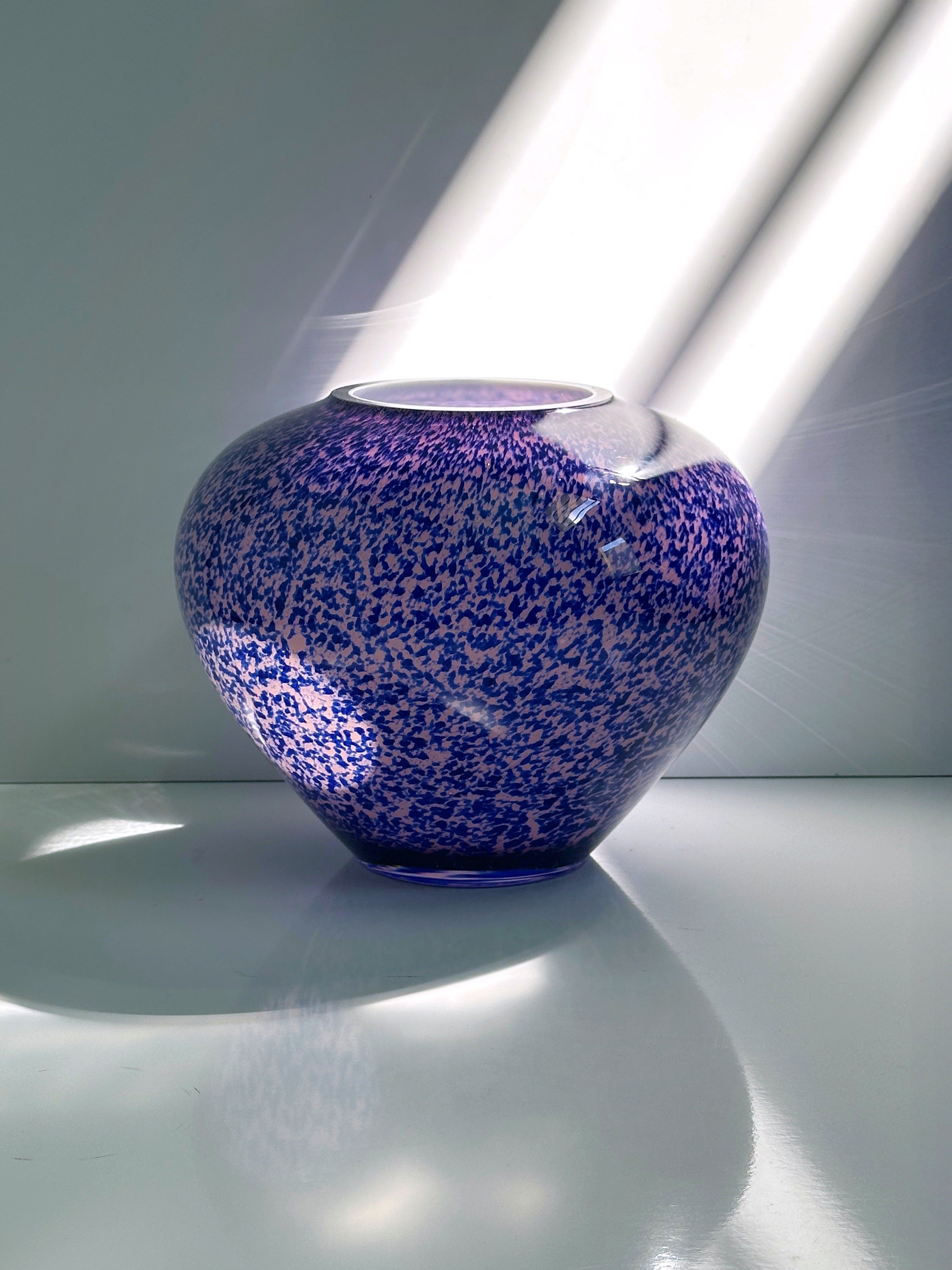 The 1930s Art Deco Tortoise Glass Vase from WMF by Dodo Vintage sits on a white surface, bathed in bright sunlight through a window that casts soft shadows and reflections.