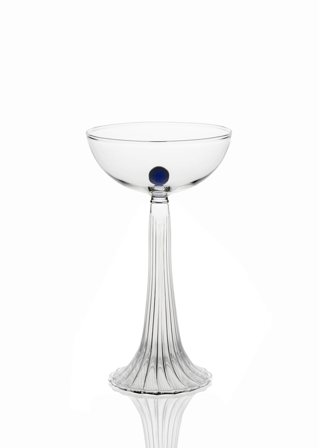 The Nereida — Coupe Glass by Agustina Bottoni is a clear handmade Italian glass with a ribbed stem and base, highlighted by a single blue dot at the center of the bowl, displayed against a plain white background.