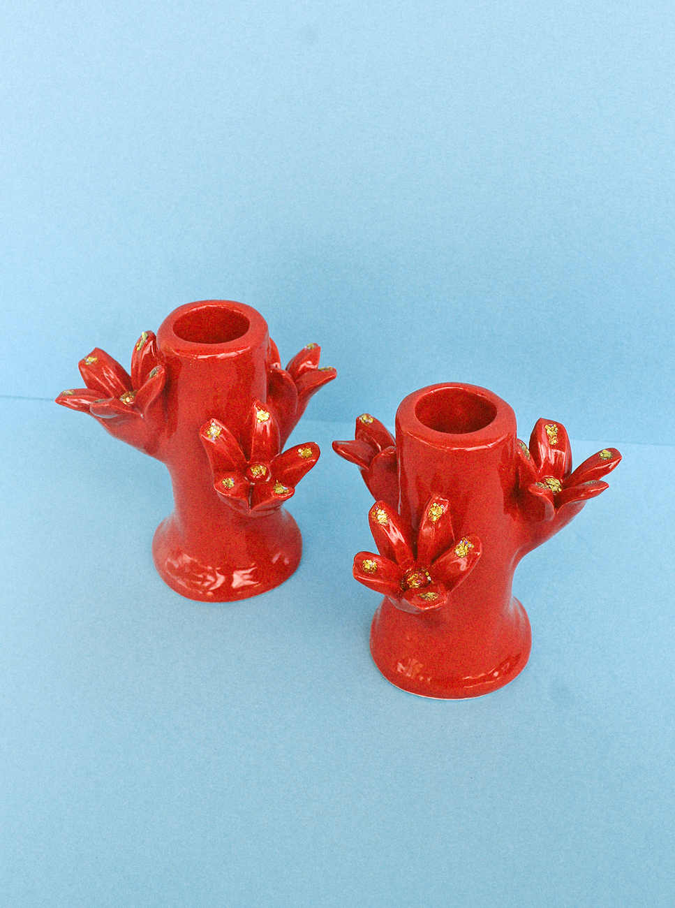 Two Flores Candleholder Set - Rojo from Casa Veronica, shaped like blooming flowers with petals, on a blue background.