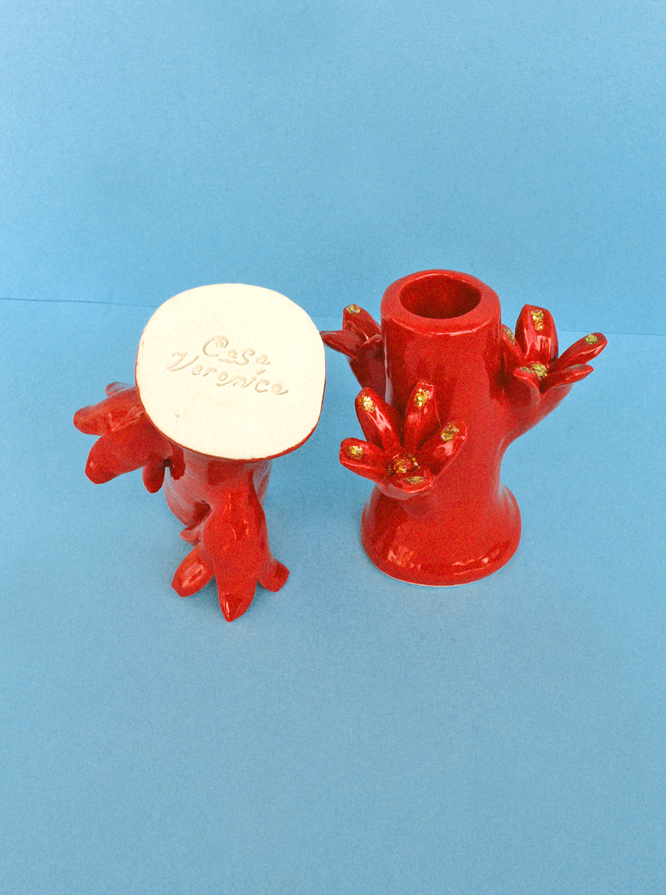 Two Flores Candleholder Set - Rojo designed with frog legs and golden accents on a blue background, one with a lid labeled "Casa Veronica.