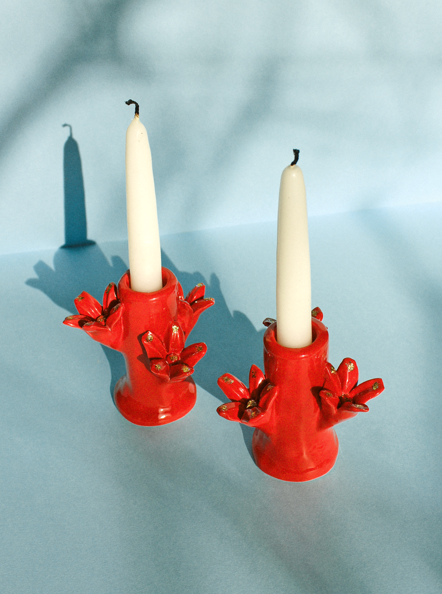 Two Flores Candleholder Sets - Rojo by Casa Veronica, each with a white candle, on a surface under soft lighting casting gentle shadows. These handcrafted candleholders make perfect home décor gifts.