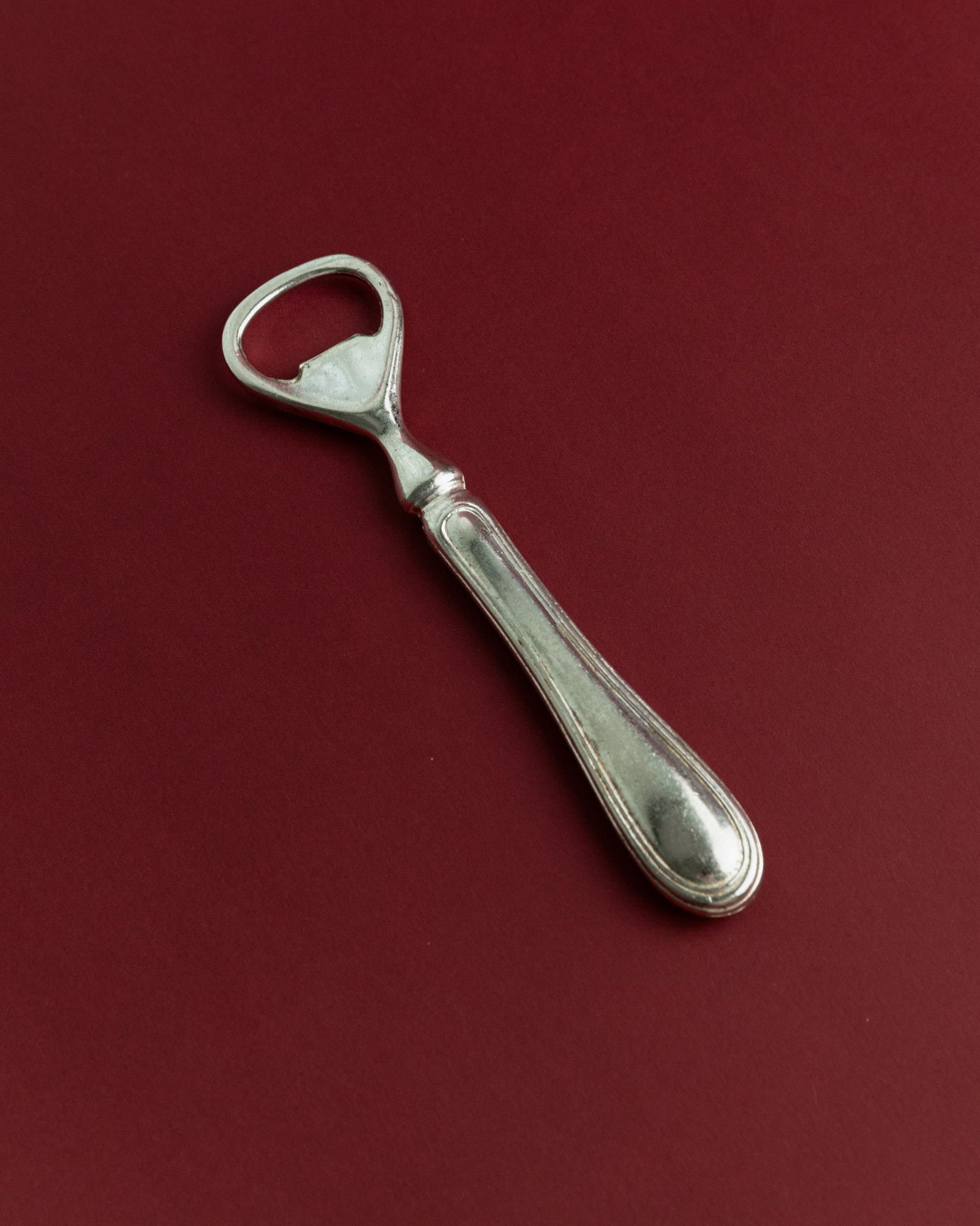 Vintage 1960s Silver Plated Bottle Opener, Classic Minimal Design, Retro Bar Accessory — angled view on burgundy background