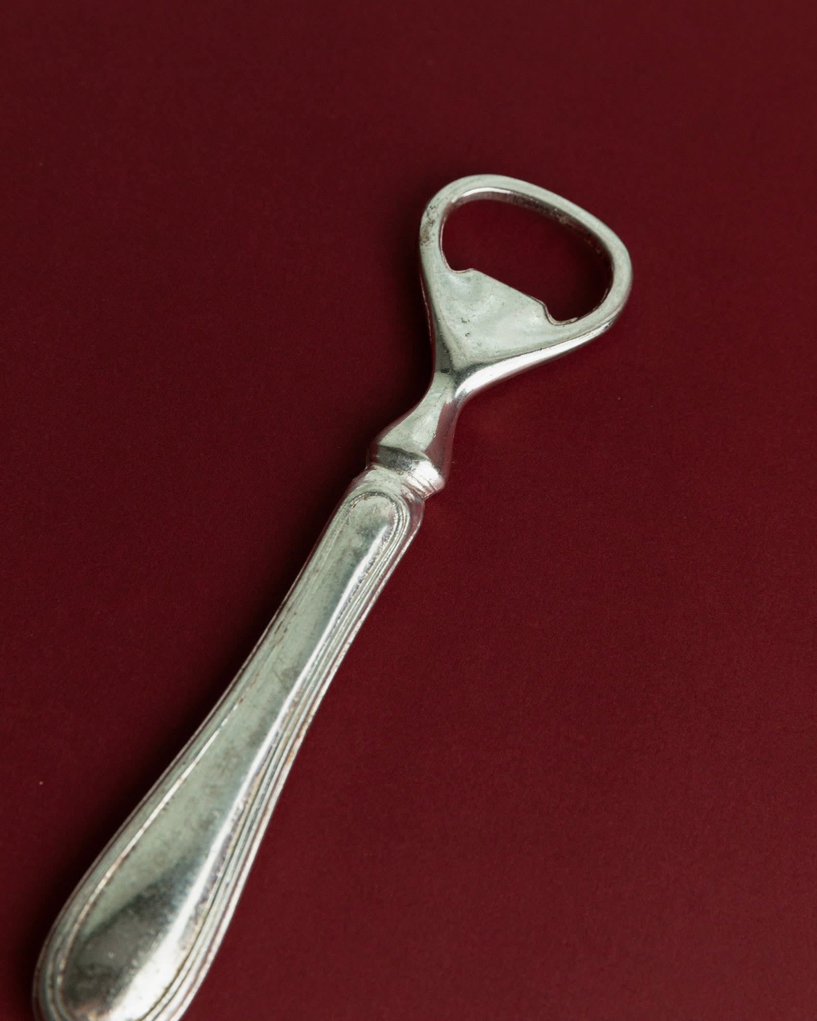 Vintage 1960s Silver Plated Bottle Opener, Classic Minimal Design — angled view on burgundy background