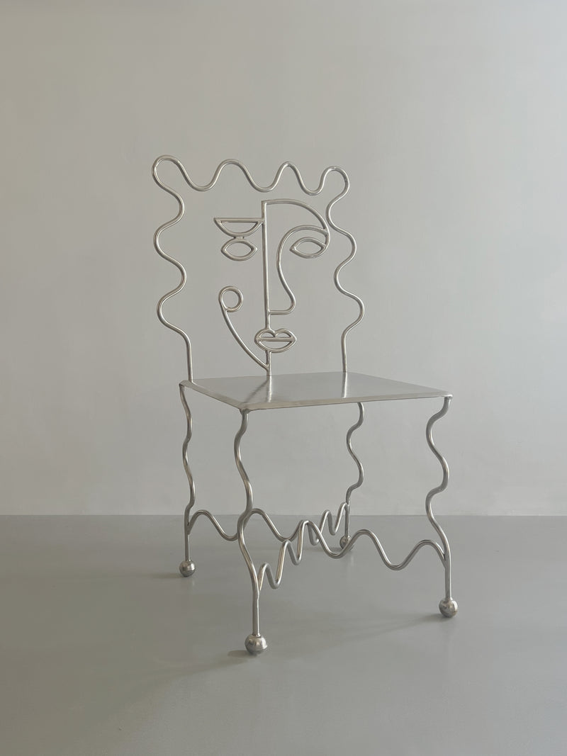 The 'M. Dupont' Chair by Zerom Studio features wavy metal legs and an abstract face line backrest, set against a plain light gray background—a limited edition collector’s piece.