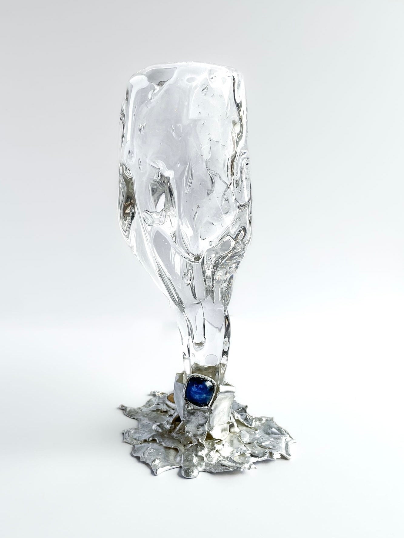 The Jewelled Goblet no. 5 by Lindsey Fontijn for Szkło Studio features clear, hand-blown textured glass atop an artistic silver base with a bold blue gemstone, showcased on a plain white background.