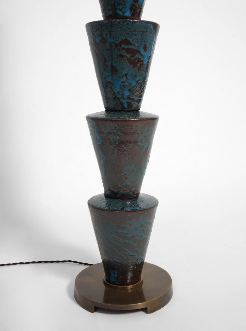 The "Nizwa" Floor Lamp by Barracuda Interiors features four stacked inverted blue and brown glazed ceramic cones with a textured finish on a round brass-colored base, plus a twisted black cord for customizable lighting.