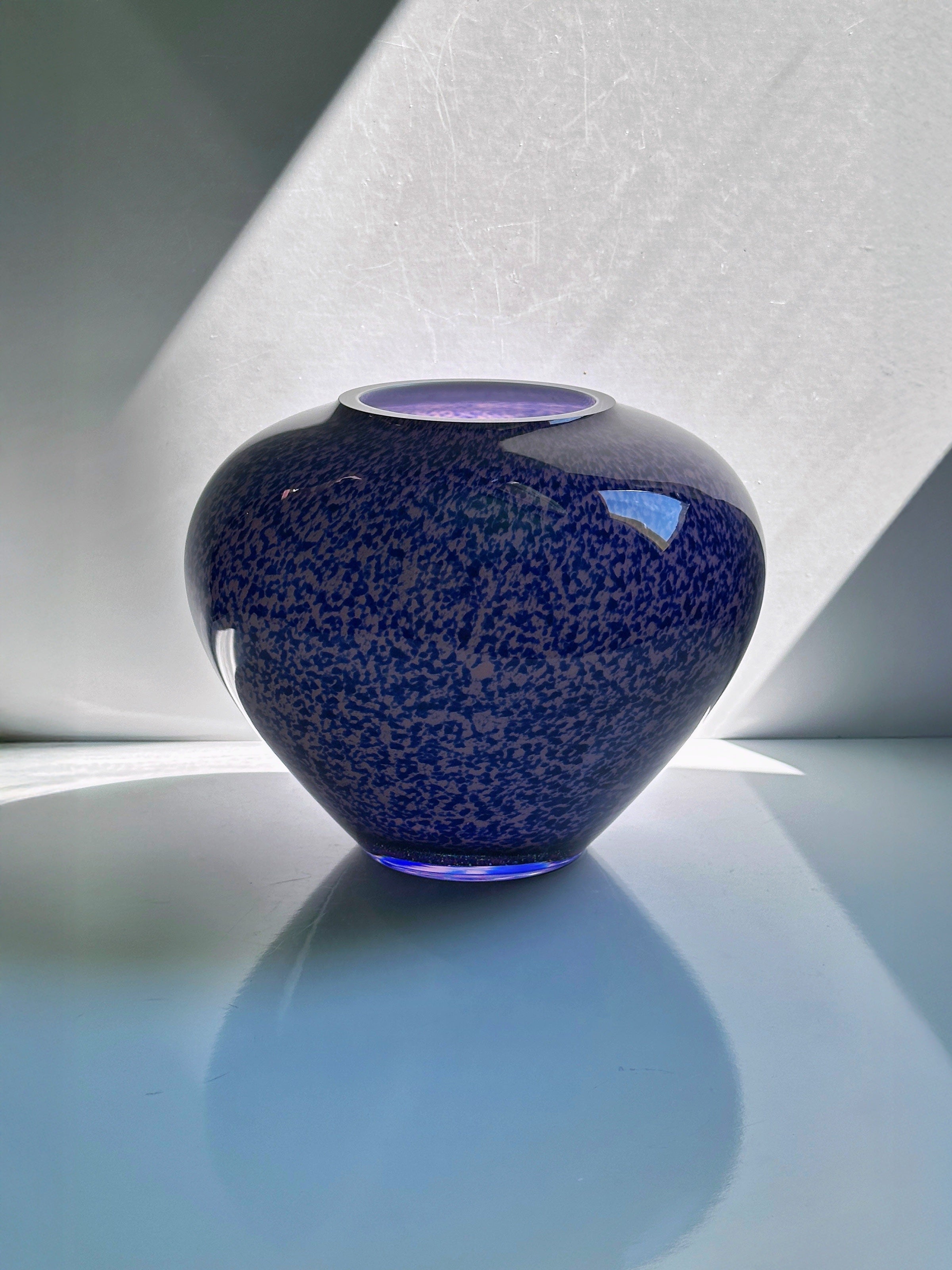 The 1930s Art Deco Tortoise Glass Vase from WMF, offered by Dodo Vintage, is centered on a white surface and illuminated by diagonal light that casts striking shadows and reflections behind and beneath it.