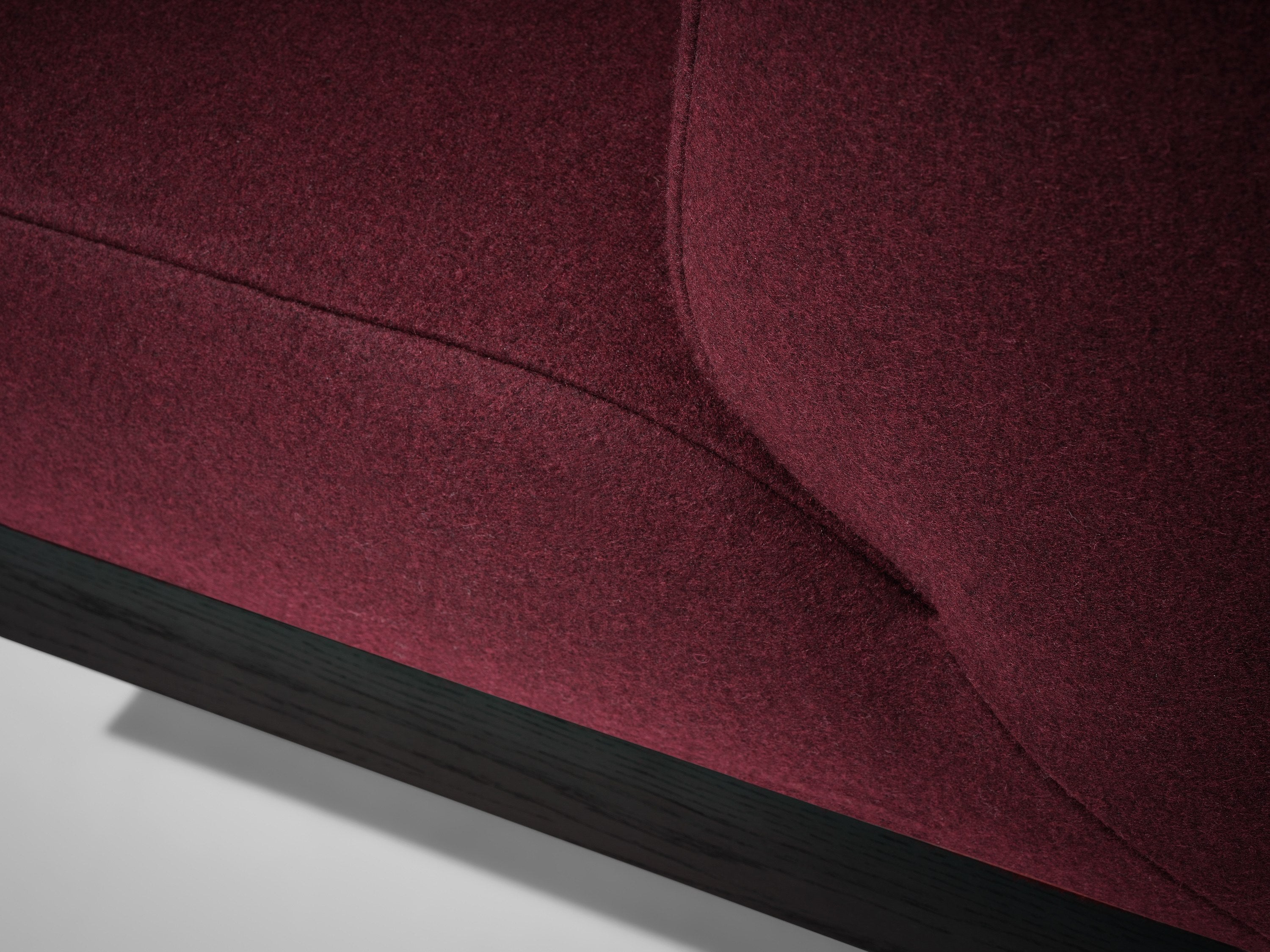 Close-up of the burgundy Mokko Acer Sofa highlighting its fabric texture, detailed seams, and sleek black wooden base against a white background—a stylish choice for any modern living room.