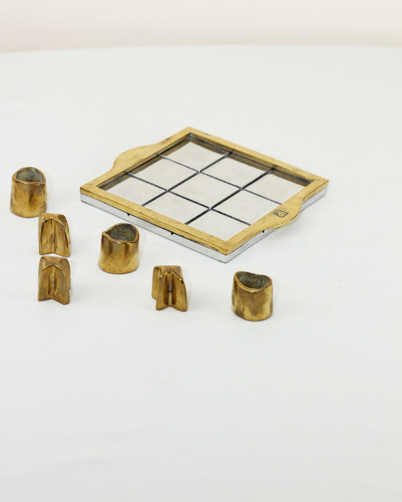 TRES EN RAYA BRUTALISTA — close-up of brass game pieces on white surface