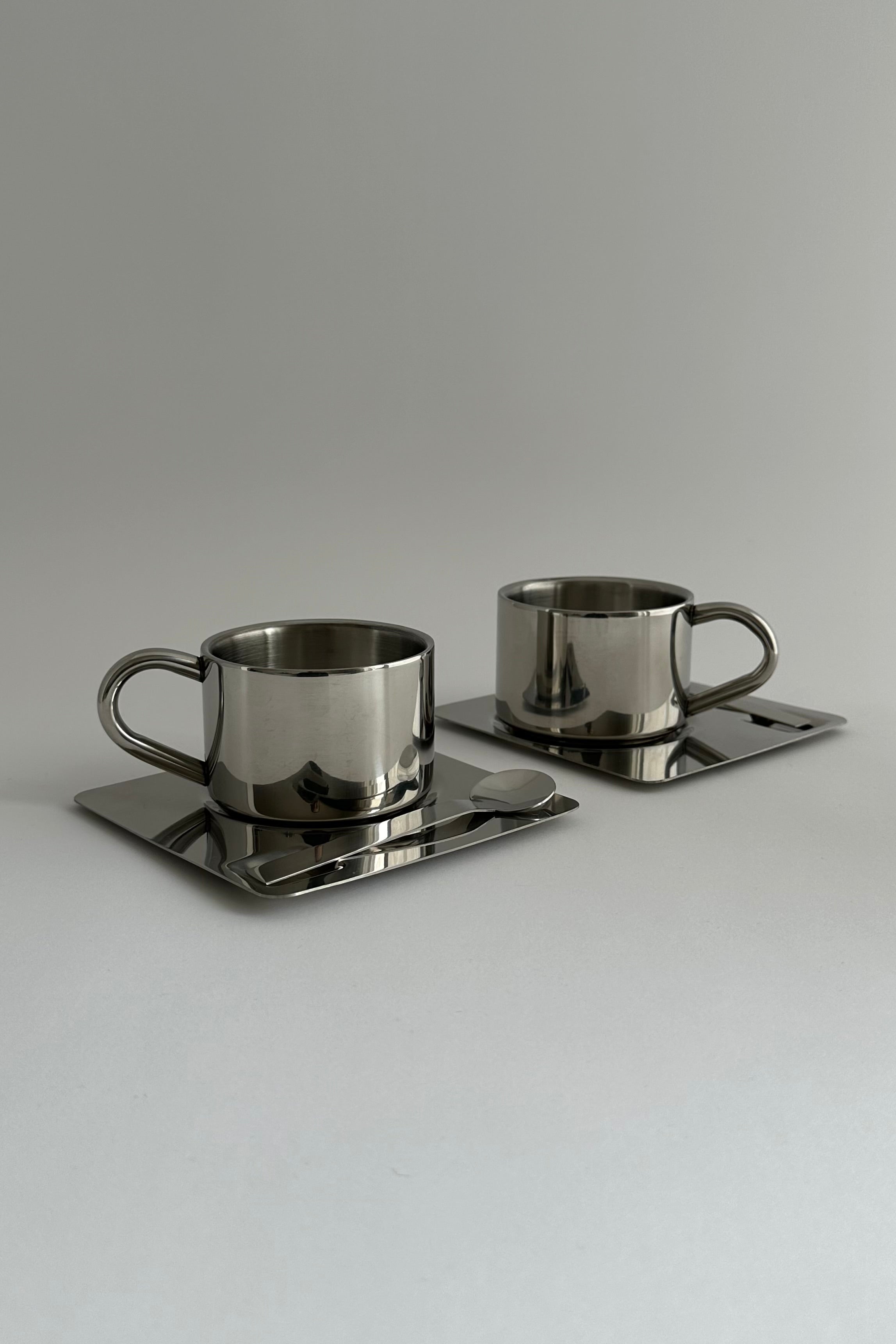 'HEDONISM' stainless steel cup with saucer — side angle