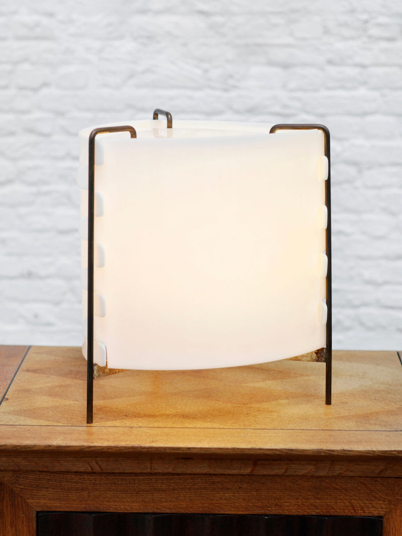 The 'M8 Fanal' lamp by Joseph-André Motte for Huchers-Minvielle (France, 1958) from Introverso features a curved frosted white shade and minimalist black metal frame, displayed on wood against a textured white brick wall.