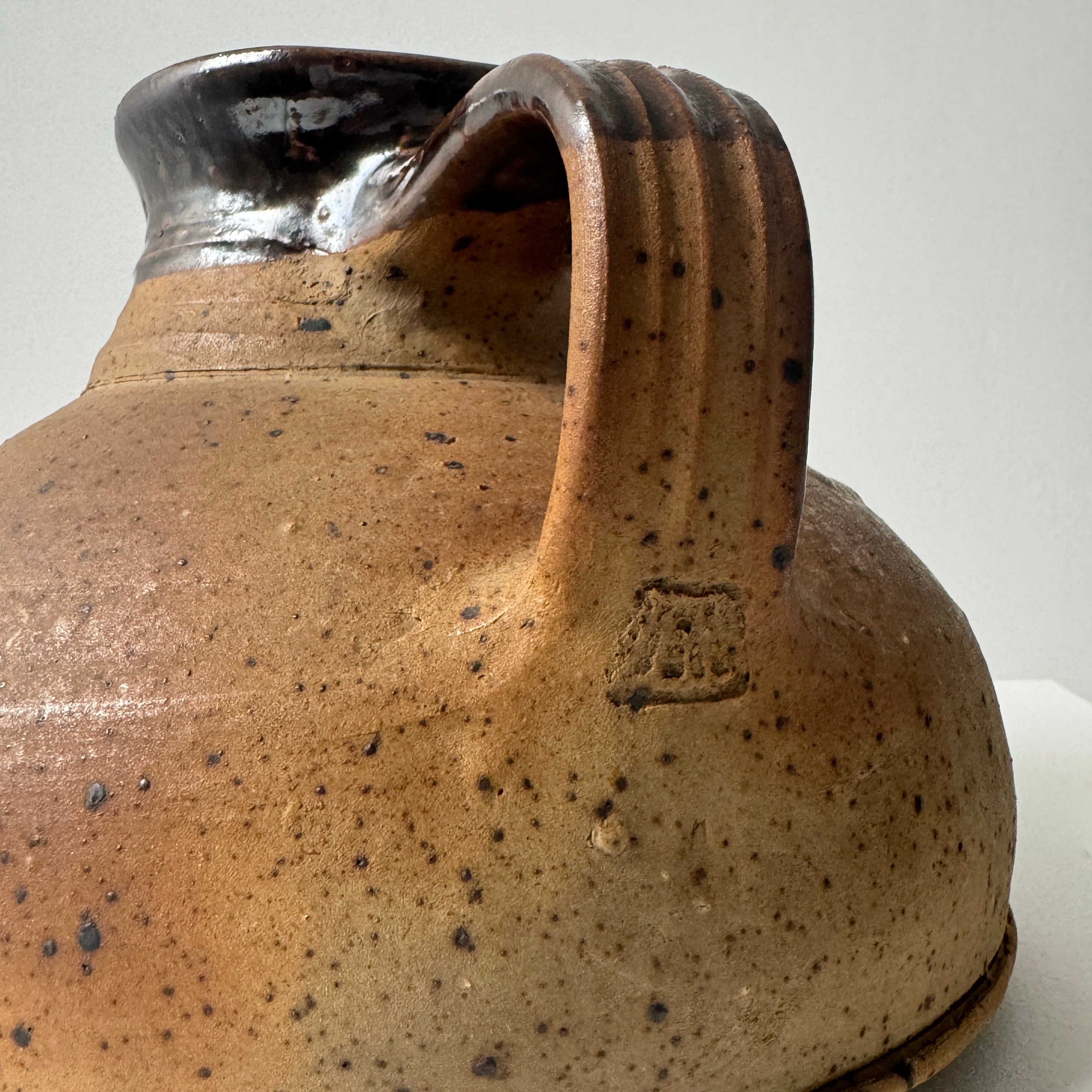 Close-up detail of speckled ceramic pitcher handle and maker's mark