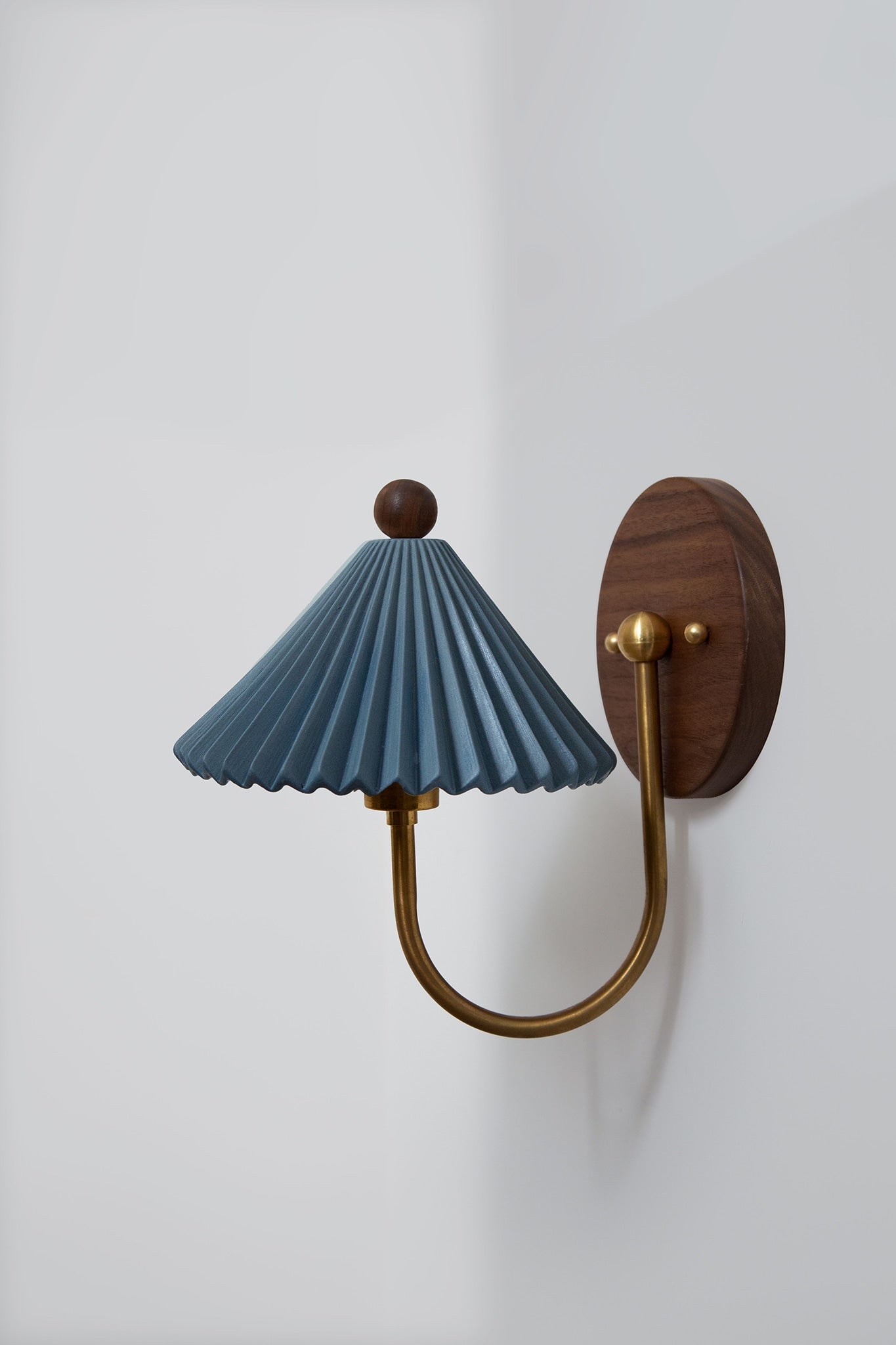Pleated teal shade wall sconce with brass arm and walnut mount