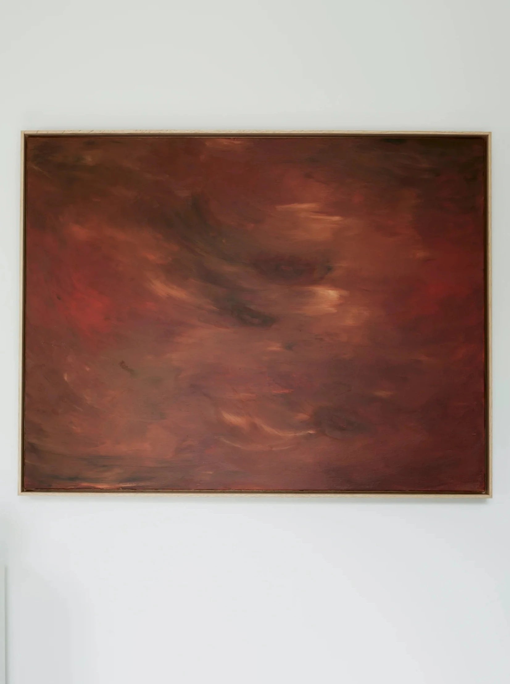 The mixed media artwork, titled "Crimson Horizons" by Mattias Storm, features a large, abstract painting with a predominantly red and brown color palette. It showcases swirls of darker and lighter shades and is part of the Terra Incognita series. Displayed in an oak frame against a white wall, it fills most of the space within the frame and boasts a textured appearance.