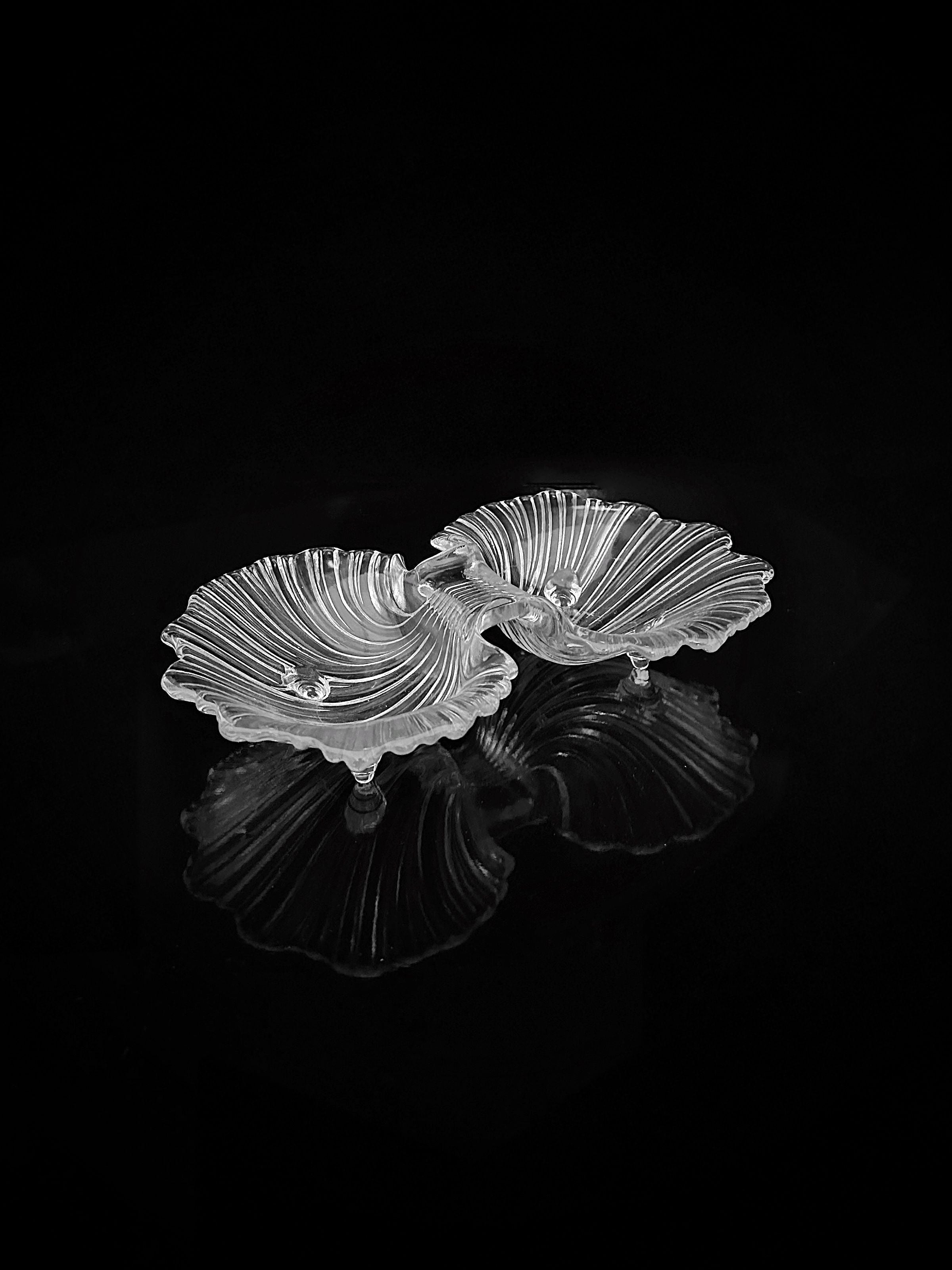Two 1980s Shell Shaped Glass Bowls by Dodo Vintage, featuring ribbed transparent glass, are displayed side by side on a glossy black surface, their reflections enhancing the elegant presentation.