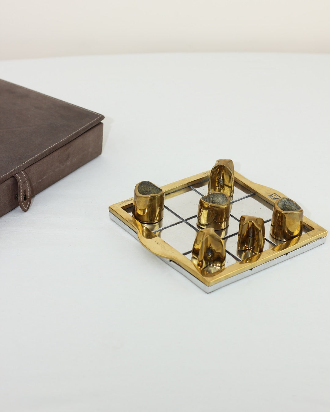 TRES EN RAYA BRUTALISTA — top view of brass and stone game pieces