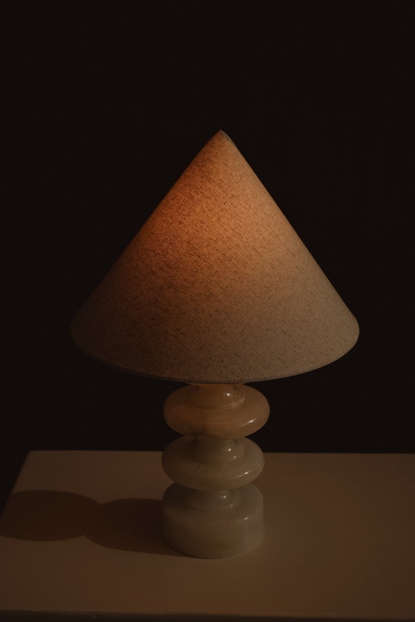 Sculptural Alabaster Table Lamp — lit conical shade in dark setting