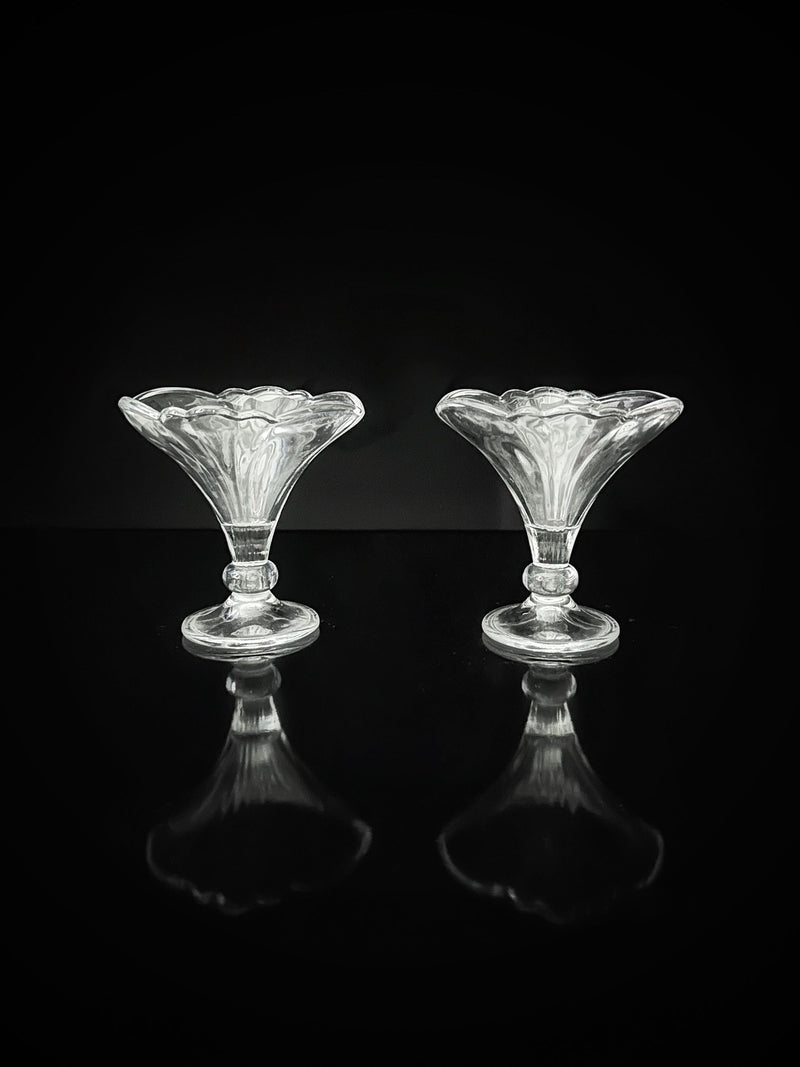 Two empty, clear Fleur-De-Lis stylised dessert cups by Dodo Vintage evoke 1980s bowls, placed side by side against a black background with glossy reflections below. Set includes 4 cups.