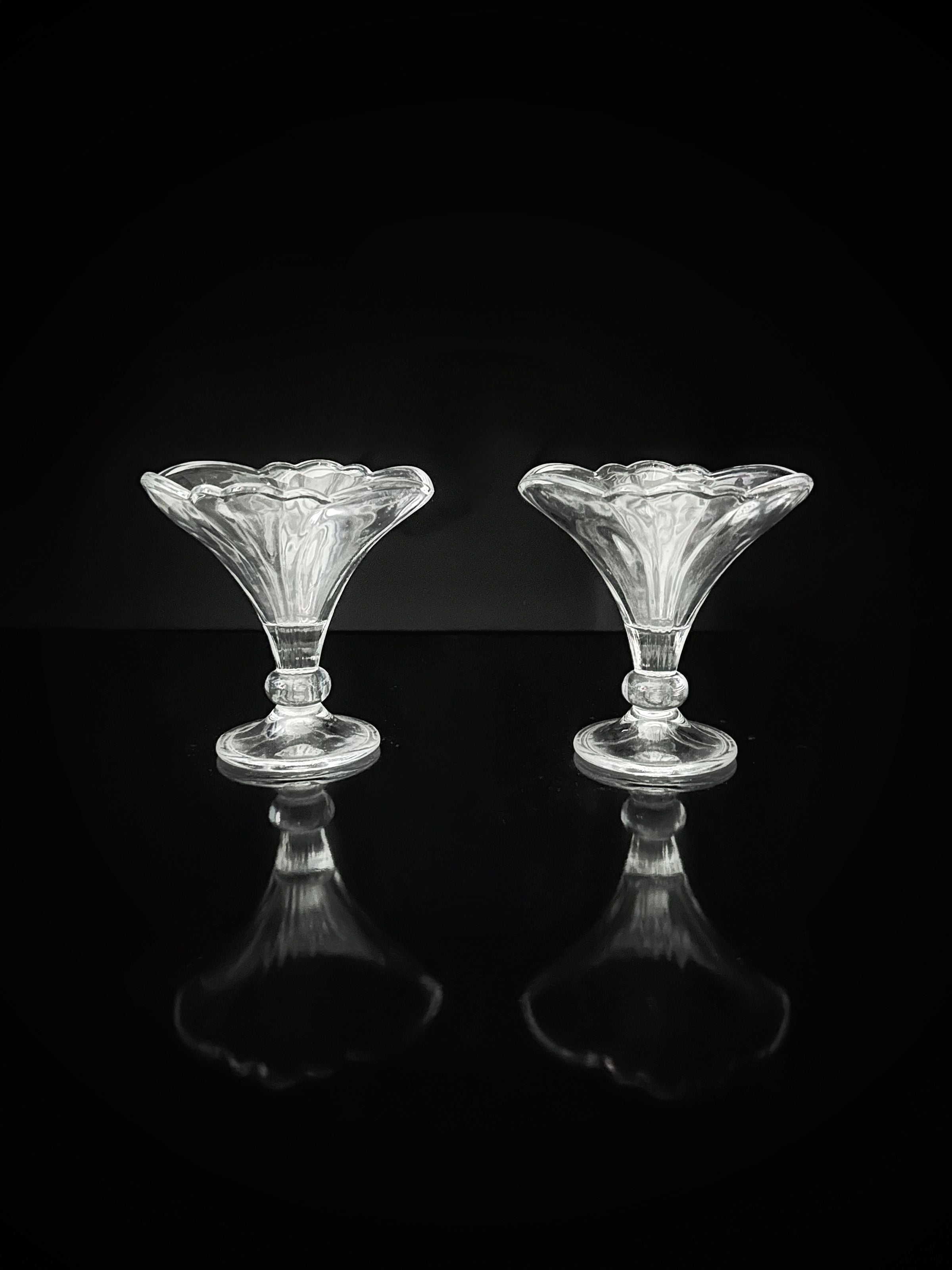 Two empty, clear Fleur-De-Lis stylised dessert cups by Dodo Vintage evoke 1980s bowls, placed side by side against a black background with glossy reflections below. Set includes 4 cups.