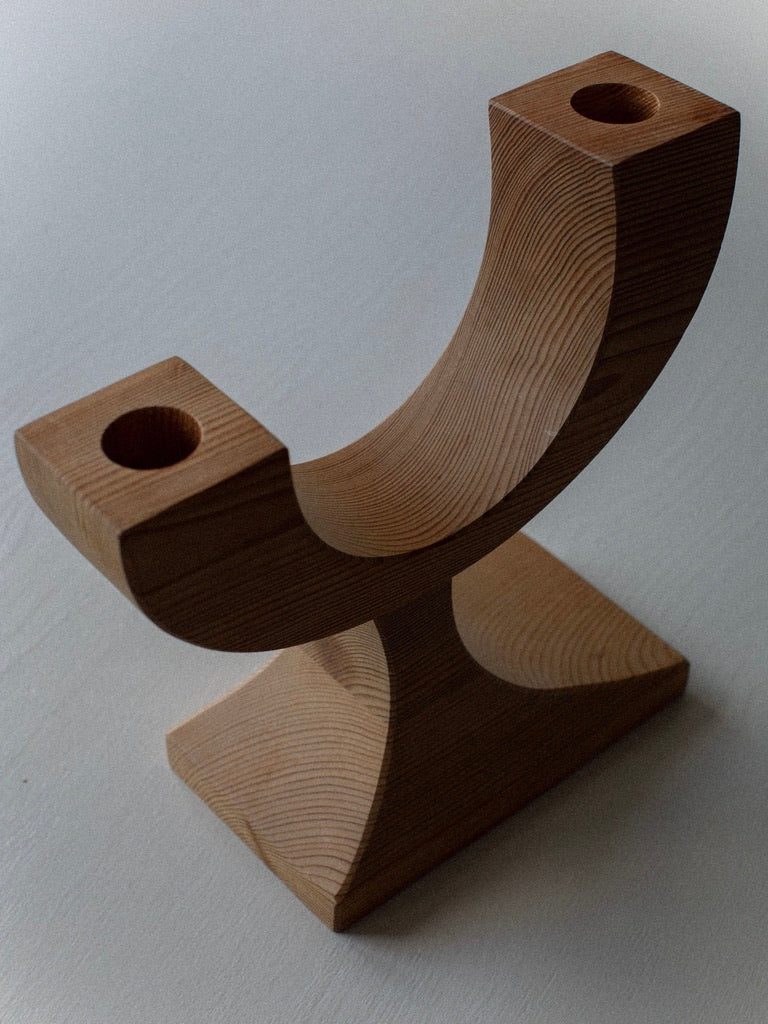 The Out For Lunch Wooden Candleholder features a curved design, rectangular base, and two square ends with circular holes. Visible wood grain highlights its vintage charm, making it a stylish pre-loved decor piece for any light surface.