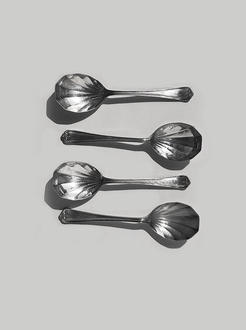 Four silver-plated shell-shaped spoons arranged on white surface