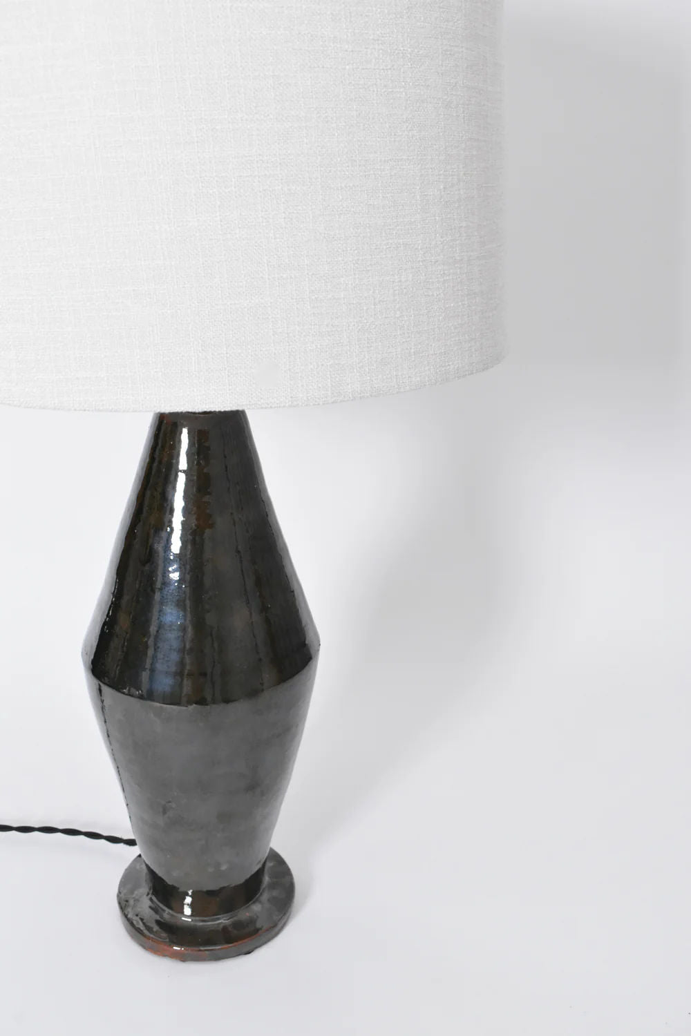 A close-up of the Arrabida Green Table Lamp by Barracuda Interiors features a textured, glossy green ceramic base with a large white fabric lampshade and black power cord, set against a plain white background. Made in Portugal.