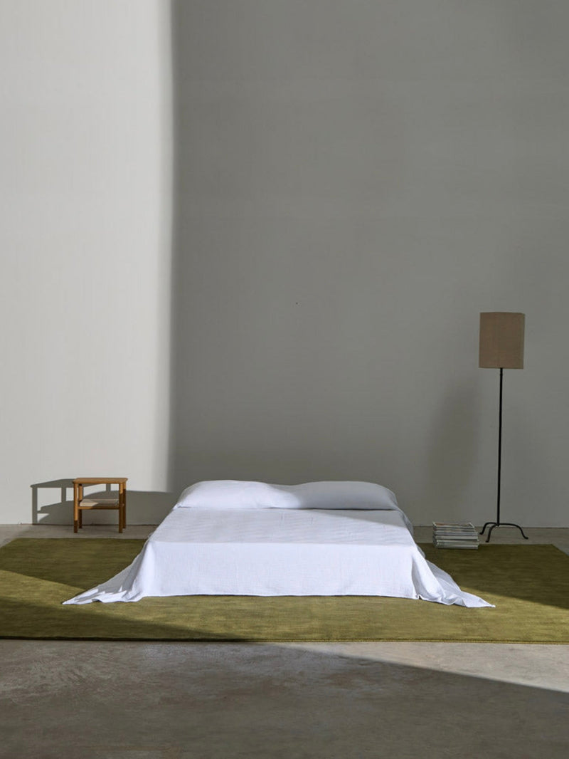 Hand-woven Rug in New Zealand Wool, Olive Green — styled under bed in minimalist bedroom