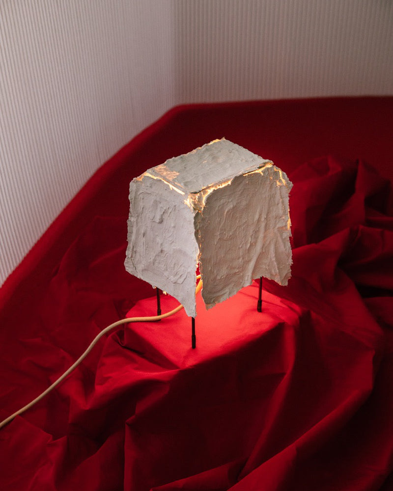 Consecuencia table lamp with illuminated stone cube on red fabric