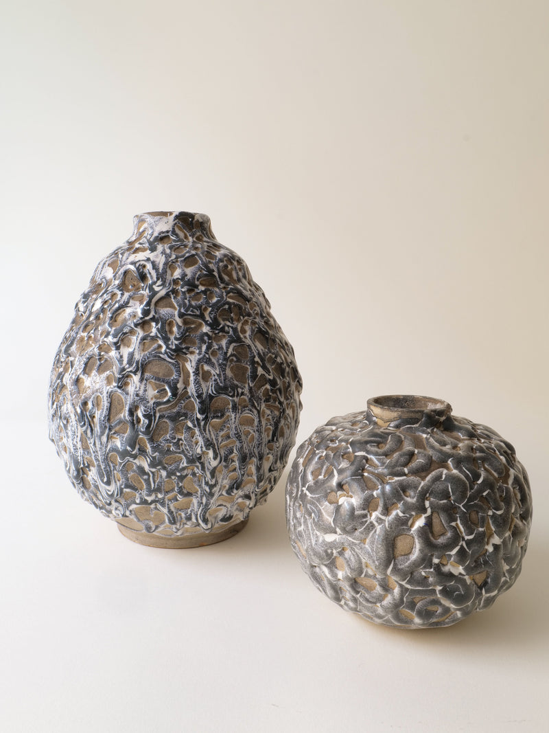 Two Deco Ceramic Vase 1930s by Collection apart, inspired by Alfred Renoleau, feature metallic, textured, organic patterns—one tall and oval, the other short and round—displayed on a neutral background.