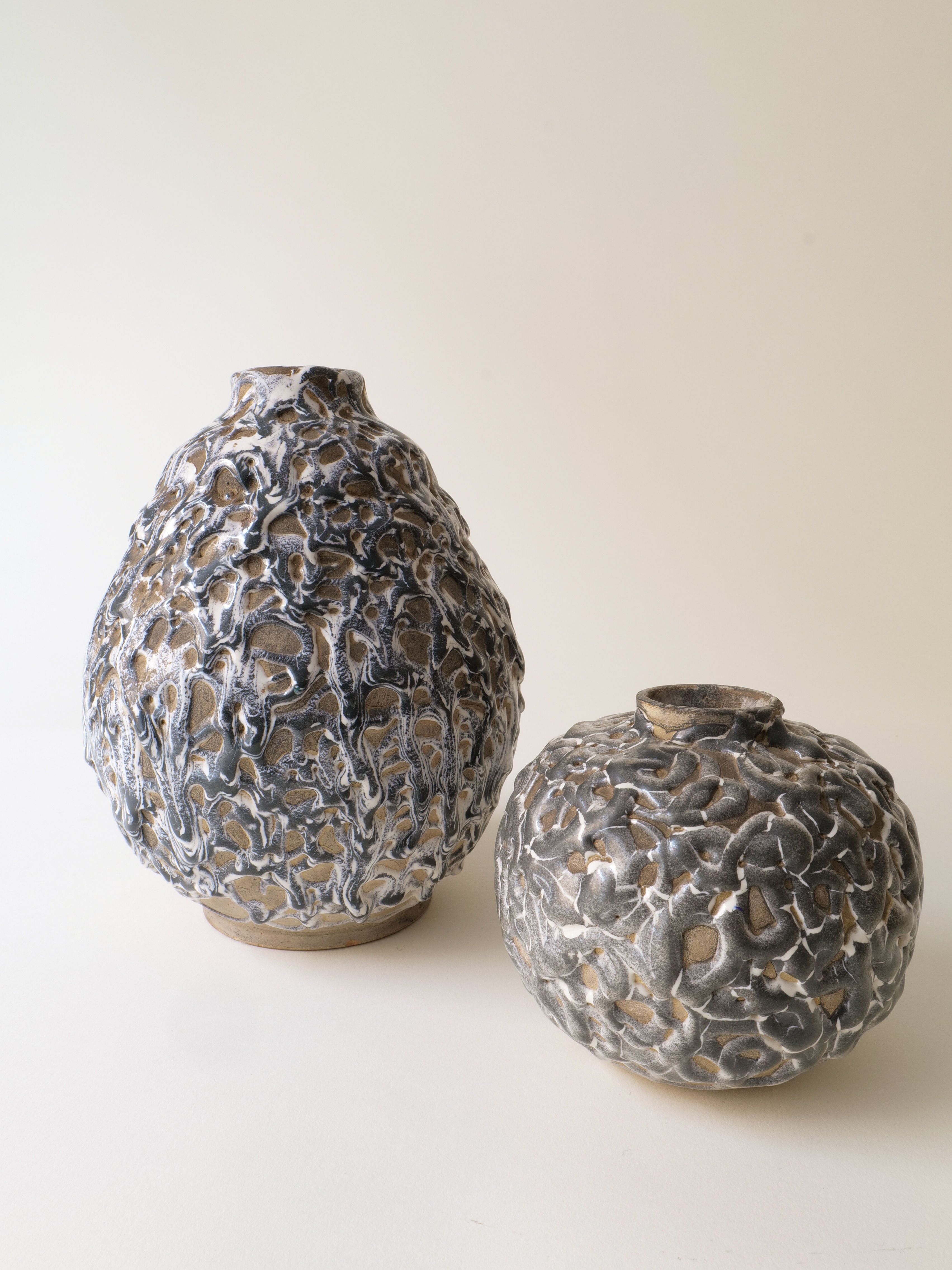 Two Deco Ceramic Vase 1930s by Collection apart, inspired by Alfred Renoleau, feature metallic, textured, organic patterns—one tall and oval, the other short and round—displayed on a neutral background.
