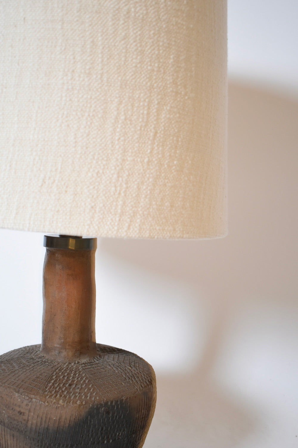 A close-up of the African Brown Ceramic Table Lamp by Barracuda Interiors, 1970s, showcasing its textured brown terracotta base with a geometric pattern and a large cream fabric lampshade against a plain white background.