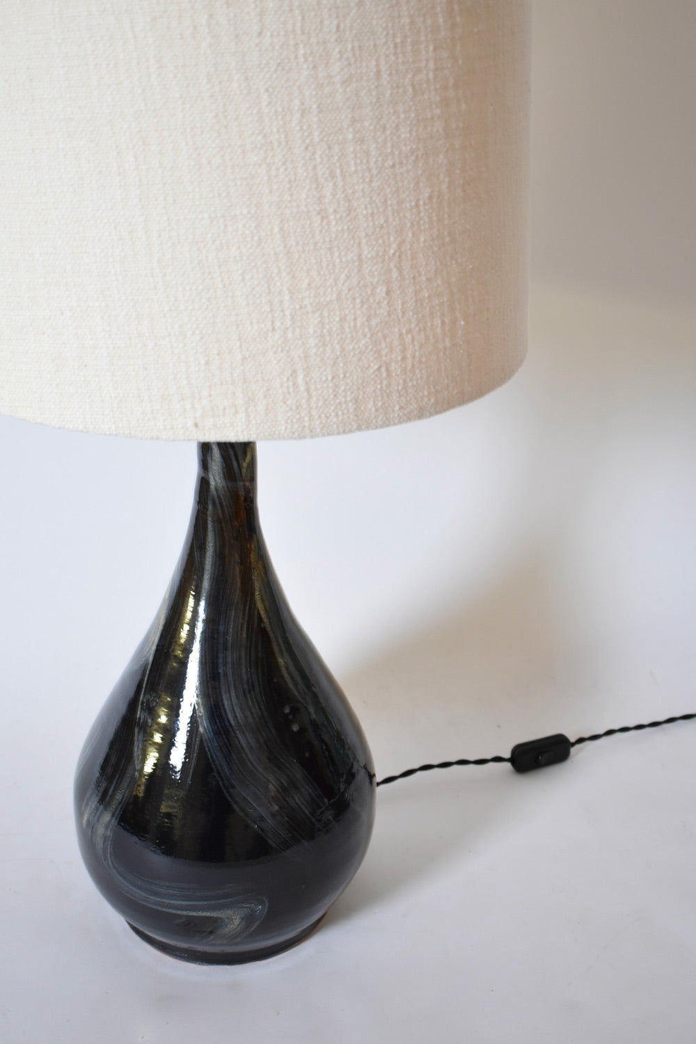 The Black Ivory Brush Lamp, Helder by Barracuda Interiors features a rounded black glass base with white swirls, a textured off-white shade, and a visible cord and switch on the white surface.