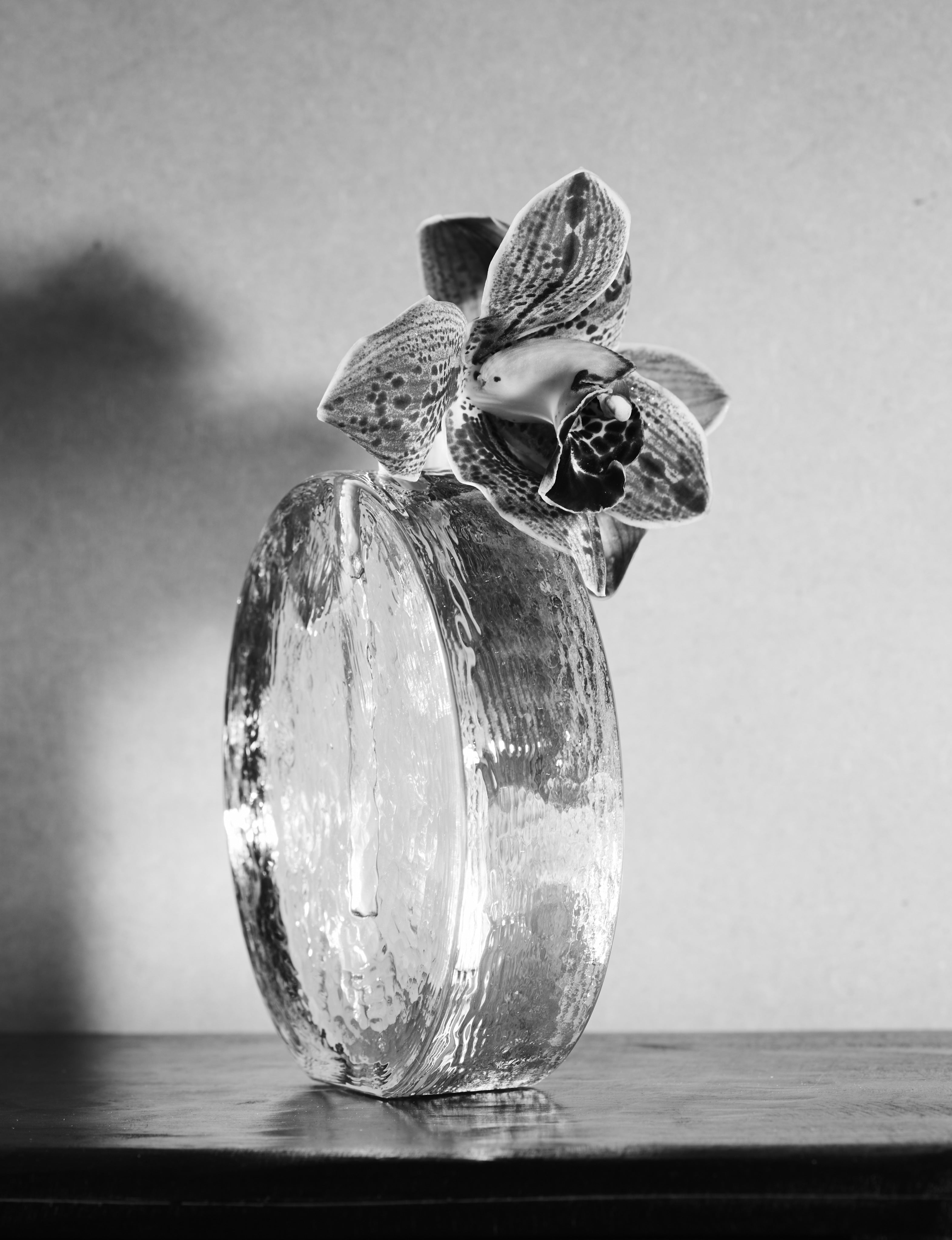 Scandinavian solifleur vase in clear glass c. 1960 — angled view with orchid on wooden surface