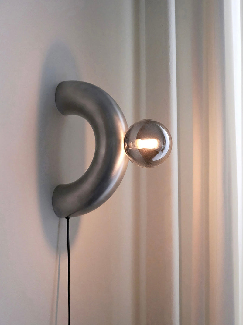 Modern aluminum arc wall lamp with glowing spherical bulb by Heako Studio