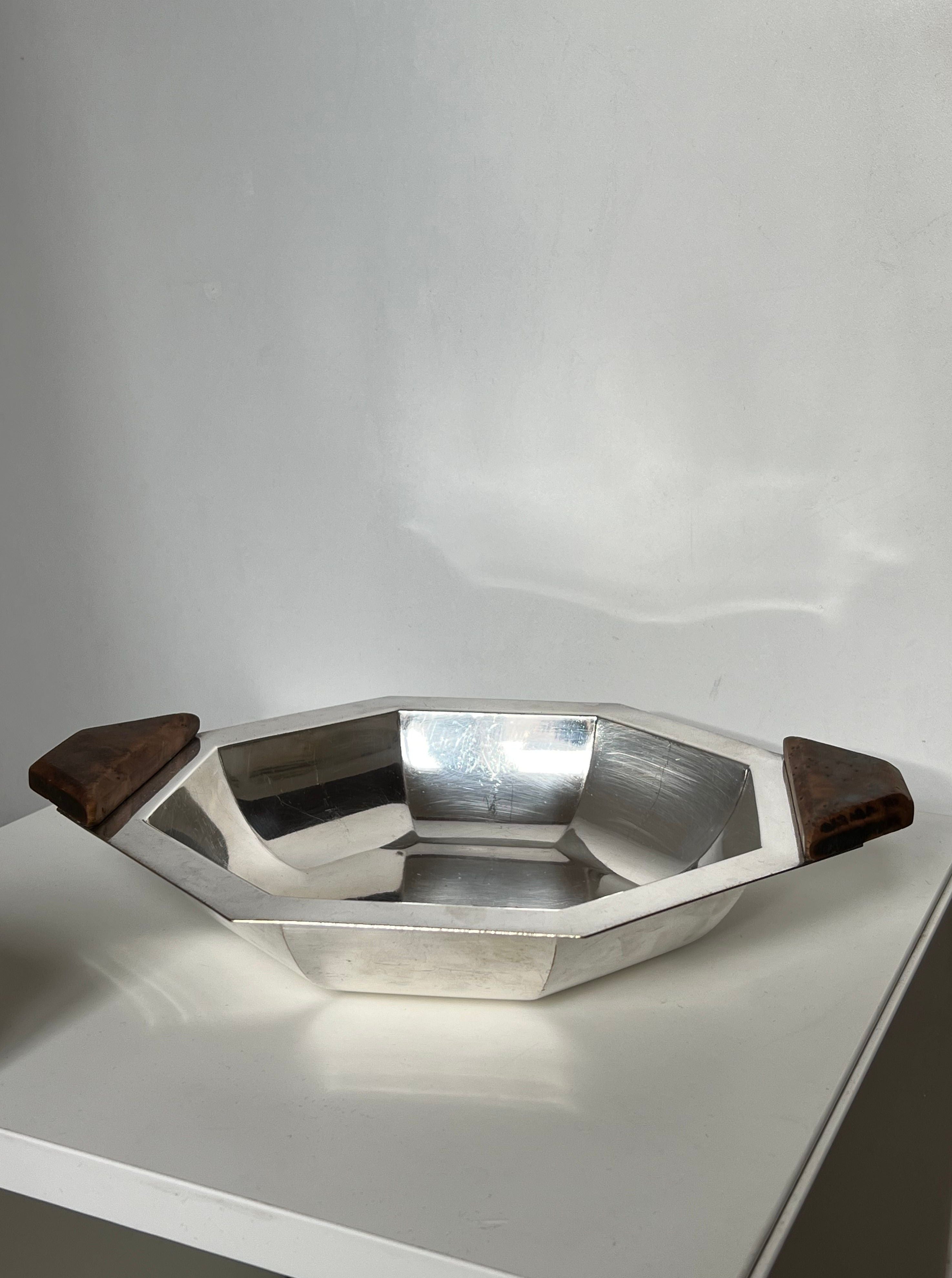 The Manushi Art Deco Decorative Dish features a shiny, octagonal design with two dark wooden handles, displayed on a white surface against a plain white background.